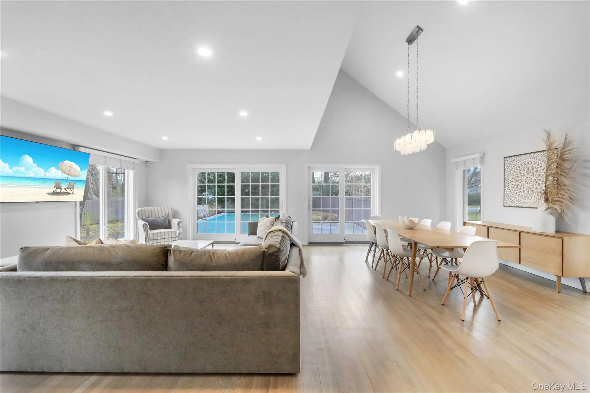 Living room featuring high vaulted ceiling, healthy amount of natural light, recessed lighting, light wood-style flooring, and a chandelier Living room featuring high vaulted ceiling, healthy amount of natural light, recessed lighting, light wood-style flooring, and a chandelier