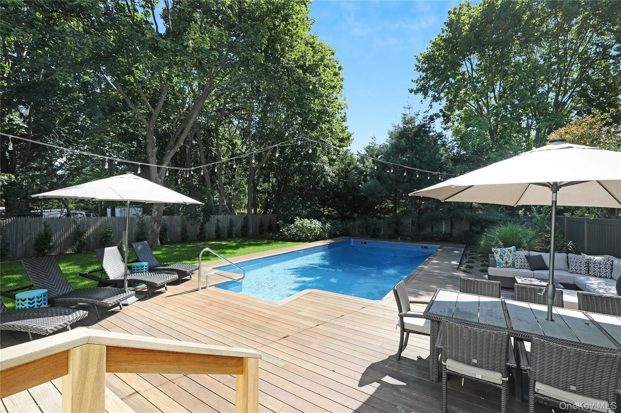 View of swimming pool featuring an outdoor hangout area, a fenced backyard, a wooden deck, view of scattered trees, and a patio area View of swimming pool featuring an outdoor hangout area, a fenced backyard, a wooden deck, view of scattered trees, and a patio area