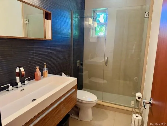 Bathroom with tile walls, a shower stall, vanity, and tile patterned floors Bathroom with tile walls, a shower stall, vanity, and tile patterned floors