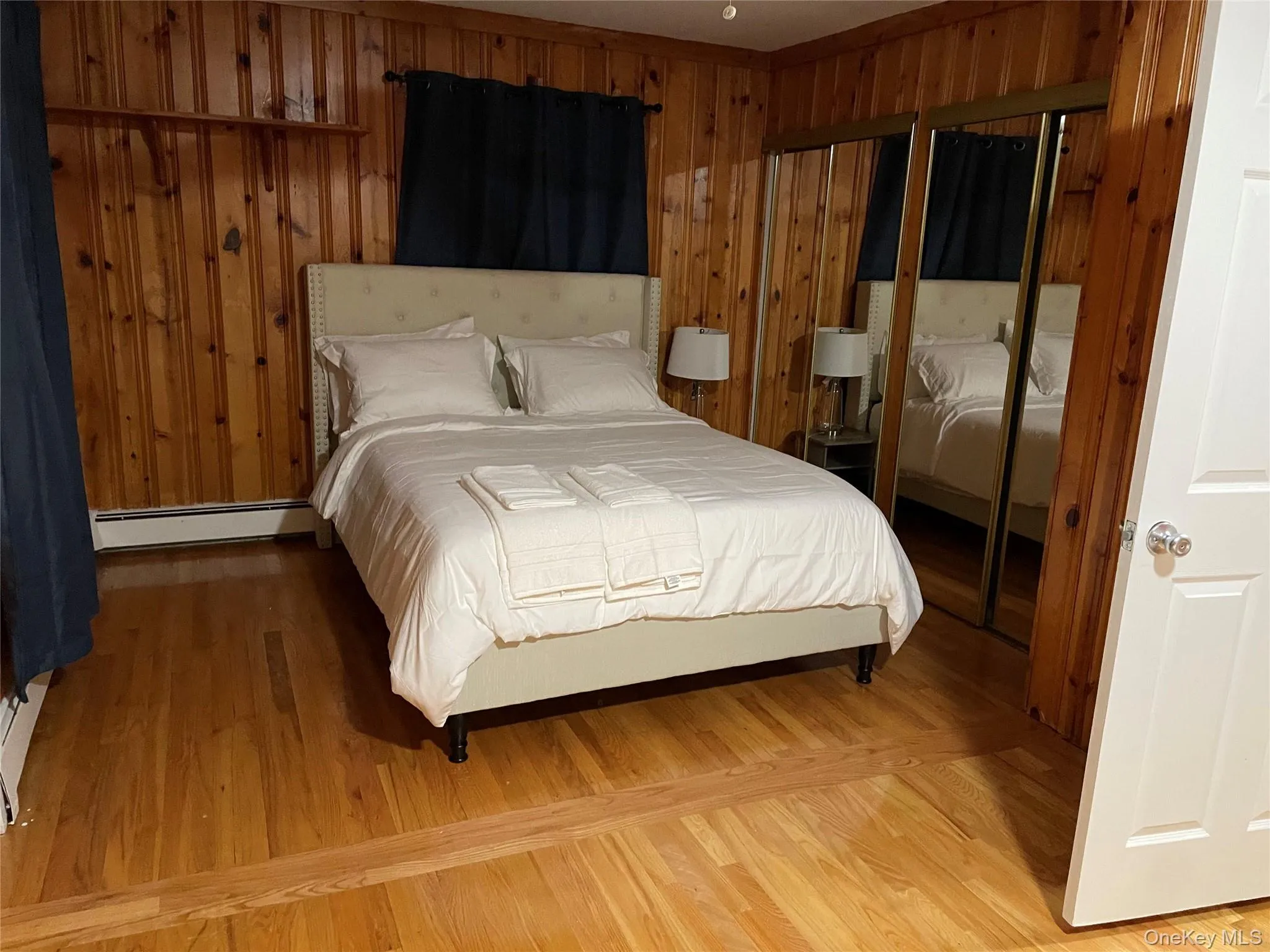 Bedroom featuring wooden walls, a closet, baseboard heating, and wood finished floors Bedroom featuring wooden walls, a closet, baseboard heating, and wood finished floors