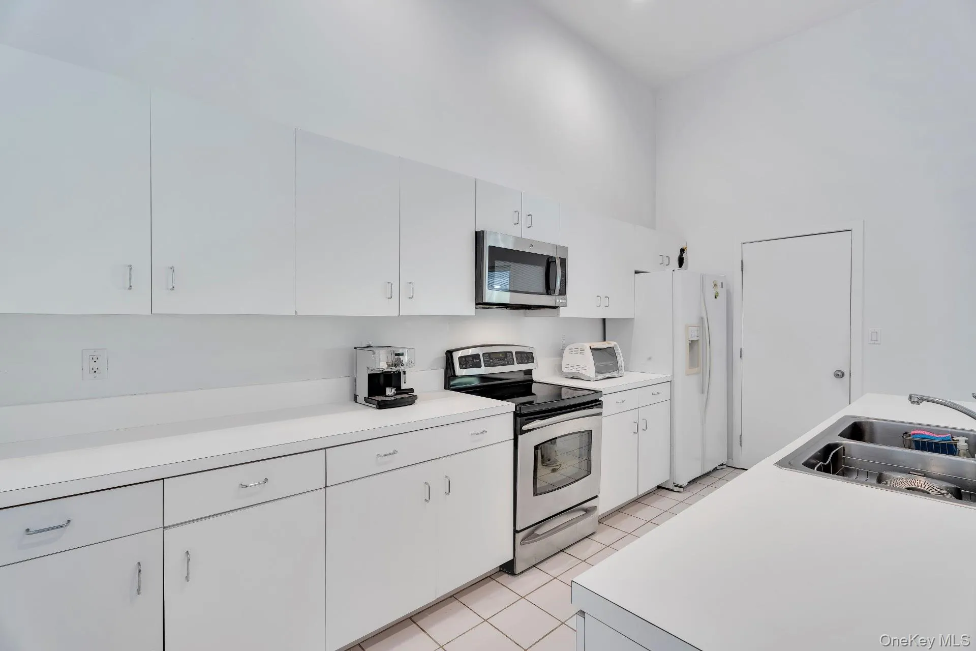 Kitchen featuring stainless steel appliances, light tile patterned floors, light countertops, white cabinets, and a high ceiling Kitchen featuring stainless steel appliances, light tile patterned floors, light countertops, white cabinets, and a high ceiling
