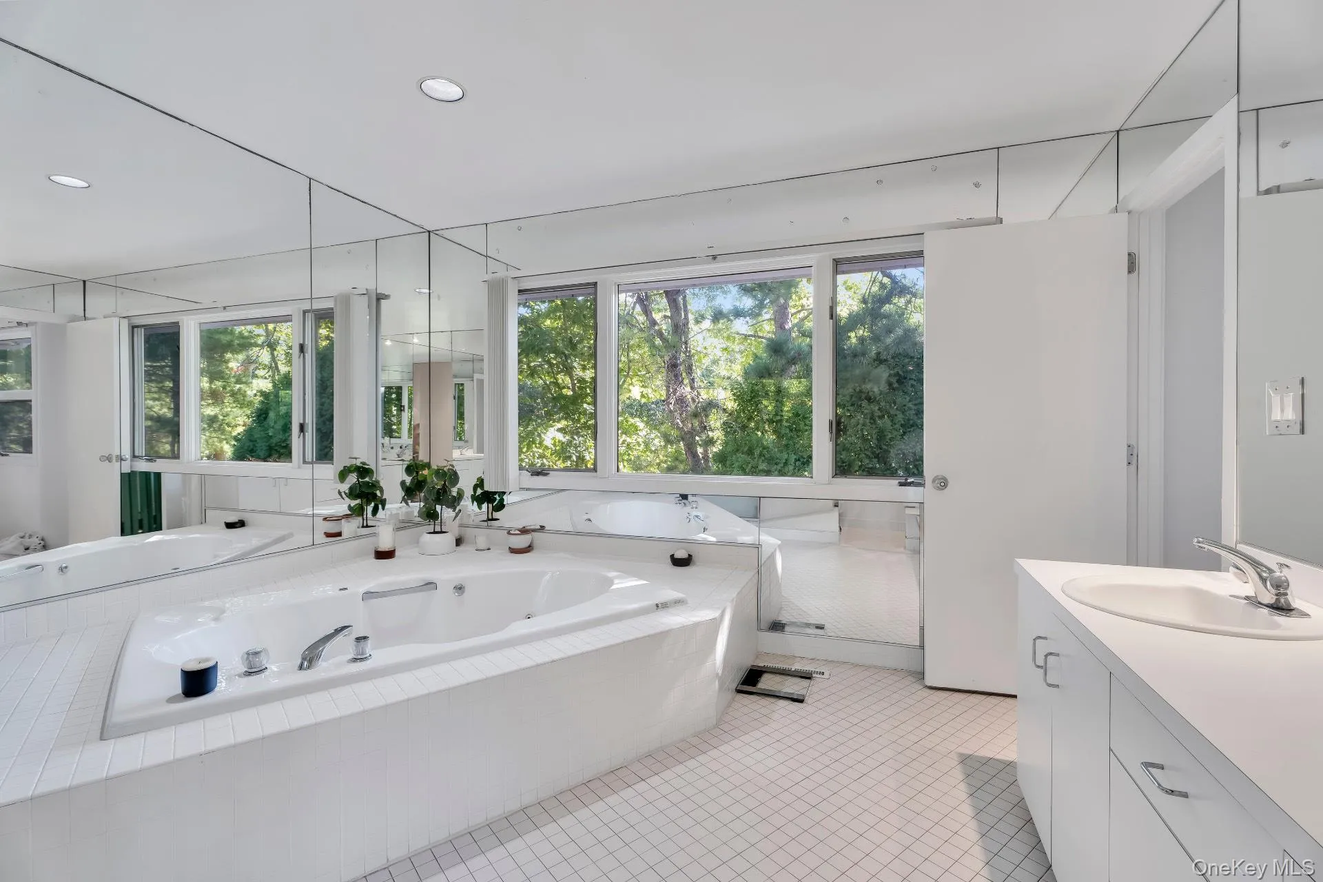 Bathroom featuring vanity, a tub with jets, light tile patterned floors, healthy amount of natural light, and recessed lighting Bathroom featuring vanity, a tub with jets, light tile patterned floors, healthy amount of natural light, and recessed lighting