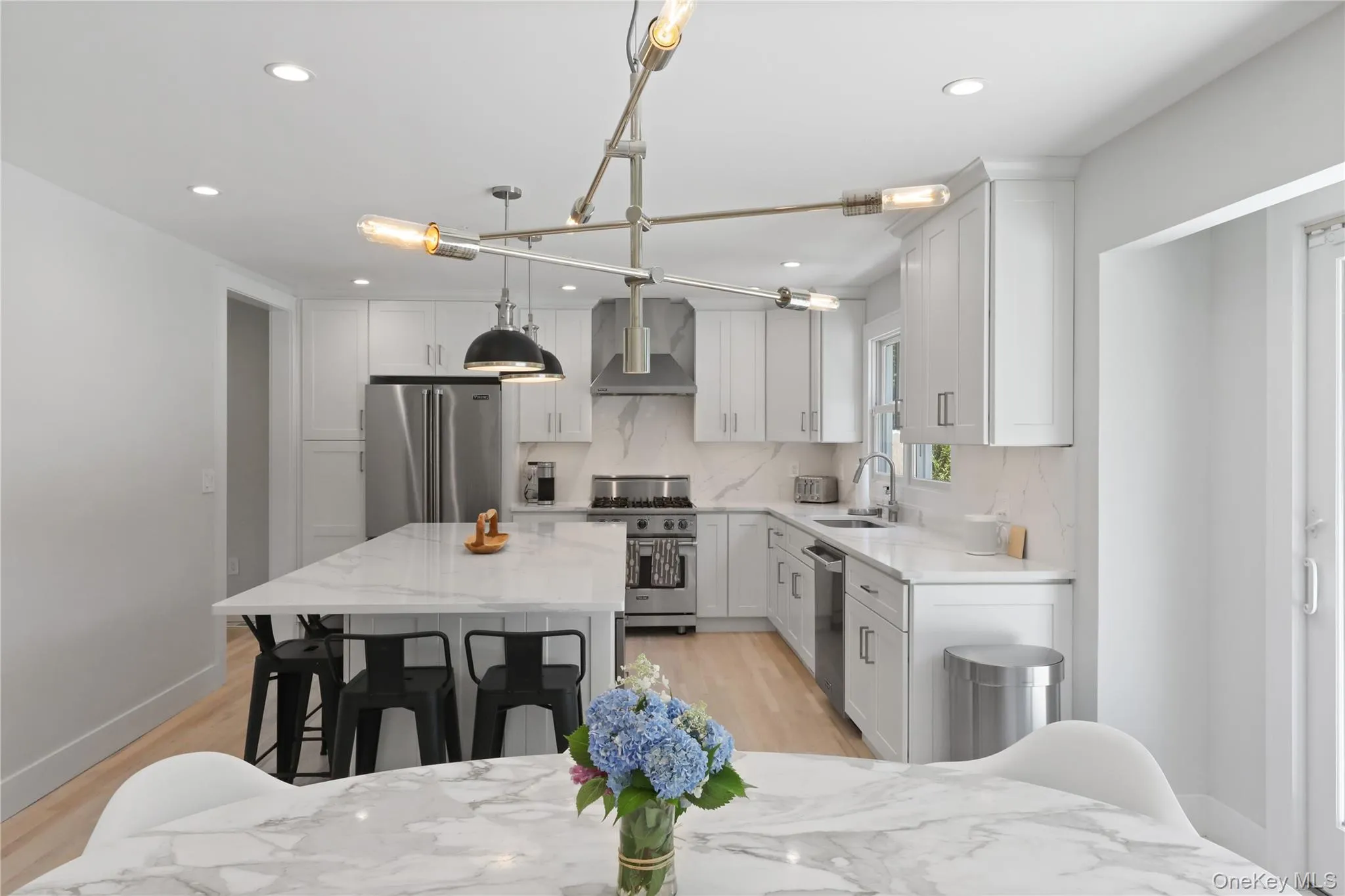 Kitchen with hanging light fixtures, wall chimney exhaust hood, high end appliances, light wood finished floors, and tasteful backsplash Kitchen with hanging light fixtures, wall chimney exhaust hood, high end appliances, light wood finished floors, and tasteful backsplash