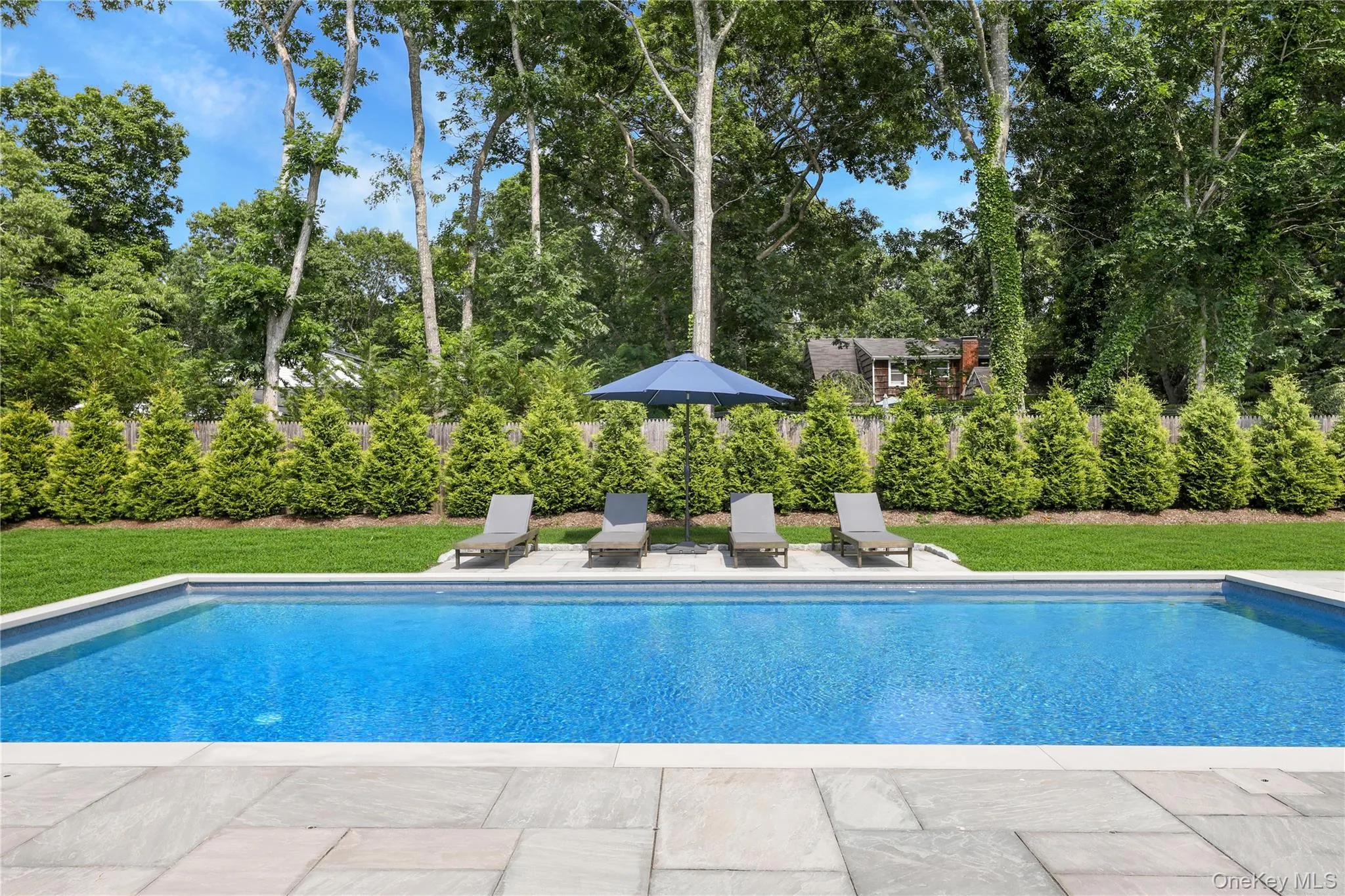 Swimming pool with a patio, a yard, and view of scattered trees Swimming pool with a patio, a yard, and view of scattered trees
