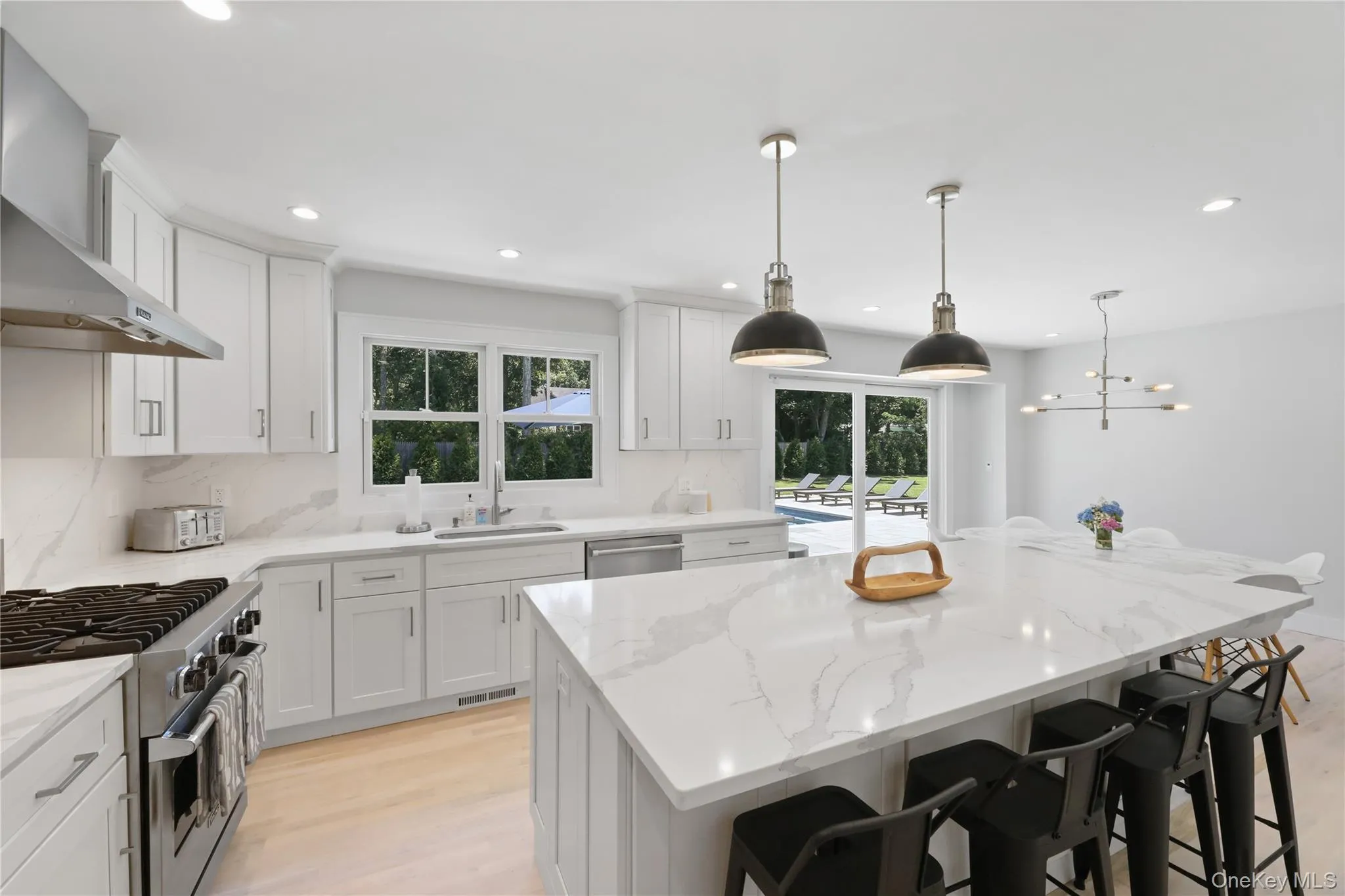 Kitchen with light wood-type flooring, stainless steel appliances, wall chimney exhaust hood, pendant lighting, and decorative backsplash Kitchen with light wood-type flooring, stainless steel appliances, wall chimney exhaust hood, pendant lighting, and decorative backsplash