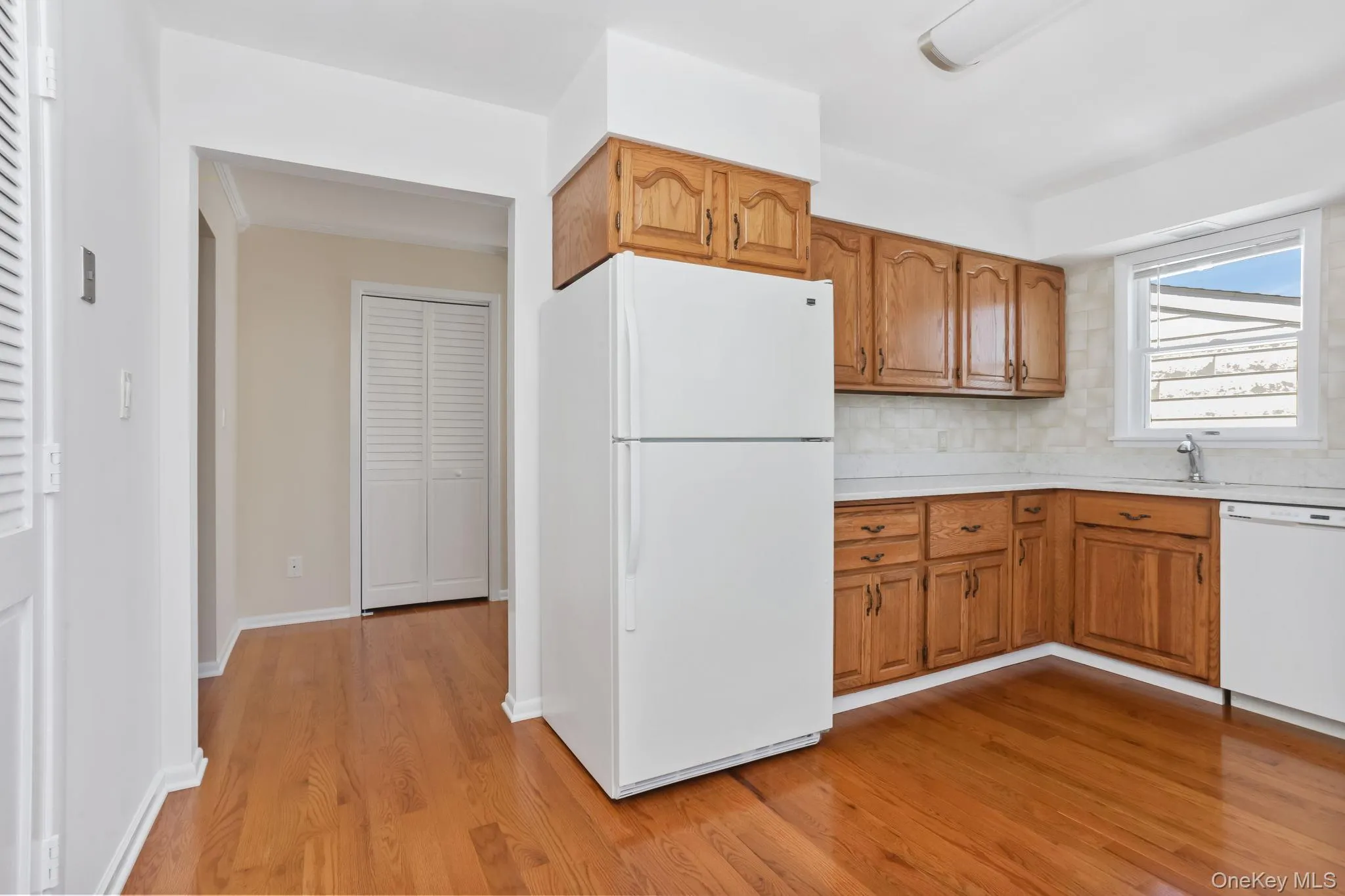 Kitchen featuring brown cabinetry, white appliances, light countertops, light wood finished floors, and tasteful backsplash Kitchen featuring brown cabinetry, white appliances, light countertops, light wood finished floors, and tasteful backsplash