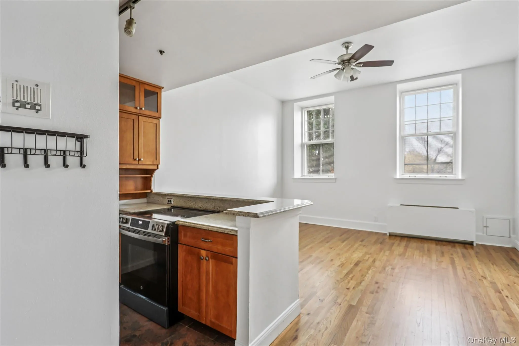 Kitchen featuring brown cabinetry, stainless steel electric range oven, radiator, and glass insert cabinets Kitchen featuring brown cabinetry, stainless steel electric range oven, radiator, and glass insert cabinets