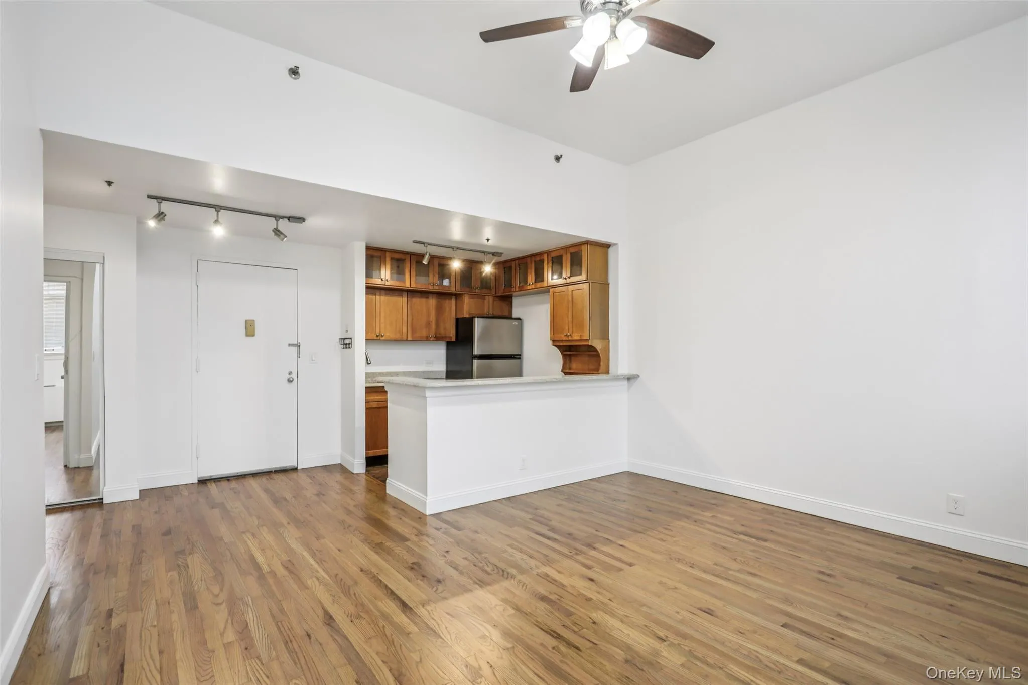 Kitchen featuring brown cabinetry, dark wood-style flooring, a peninsula, freestanding refrigerator, and light countertops Kitchen featuring brown cabinetry, dark wood-style flooring, a peninsula, freestanding refrigerator, and light countertops