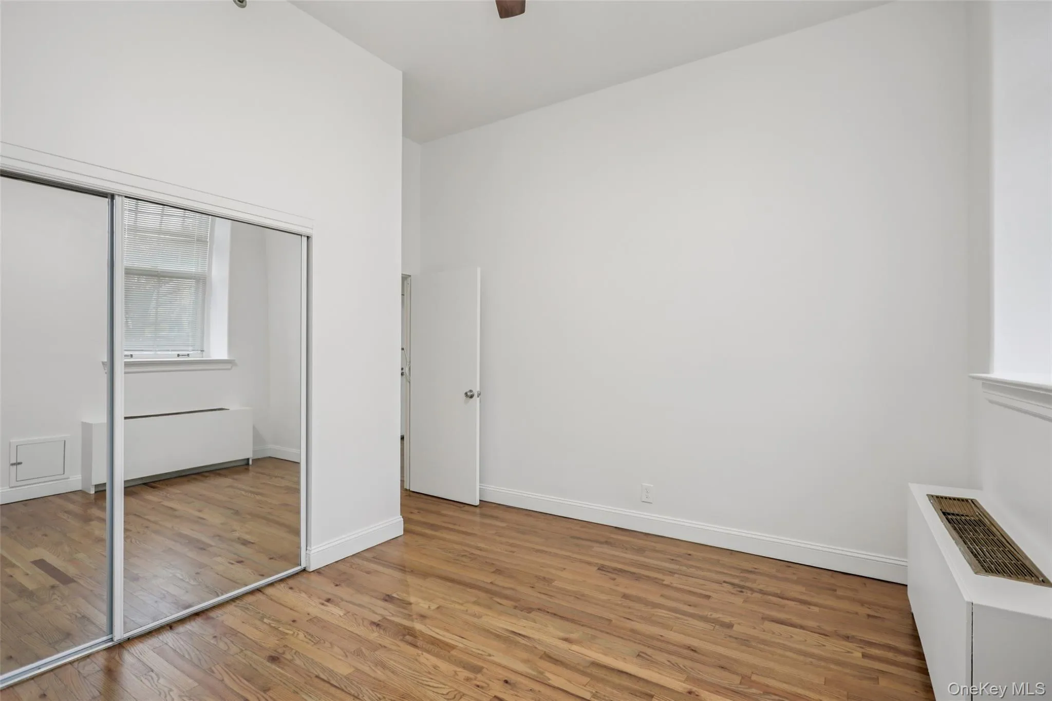 Unfurnished bedroom featuring light wood-style flooring, a closet, a ceiling fan, and radiator heating unit Unfurnished bedroom featuring light wood-style flooring, a closet, a ceiling fan, and radiator heating unit