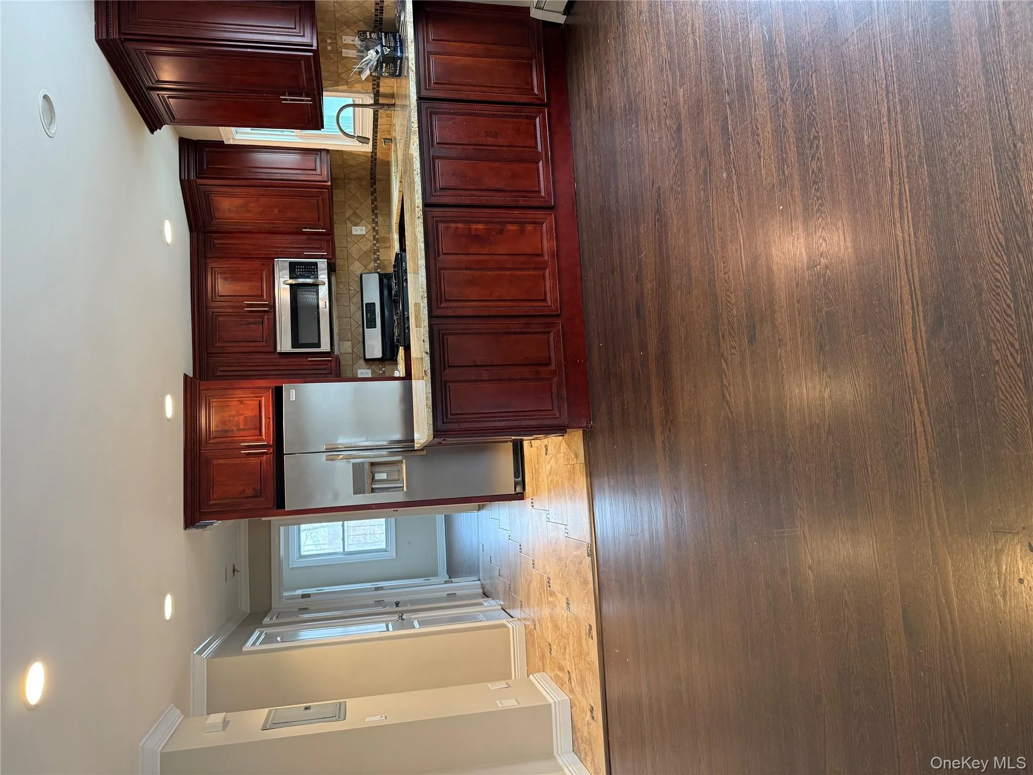 Kitchen with dark wood finished floors, refrigerator, stove, light stone countertops, and reddish brown cabinets Kitchen with dark wood finished floors, refrigerator, stove, light stone countertops, and reddish brown cabinets