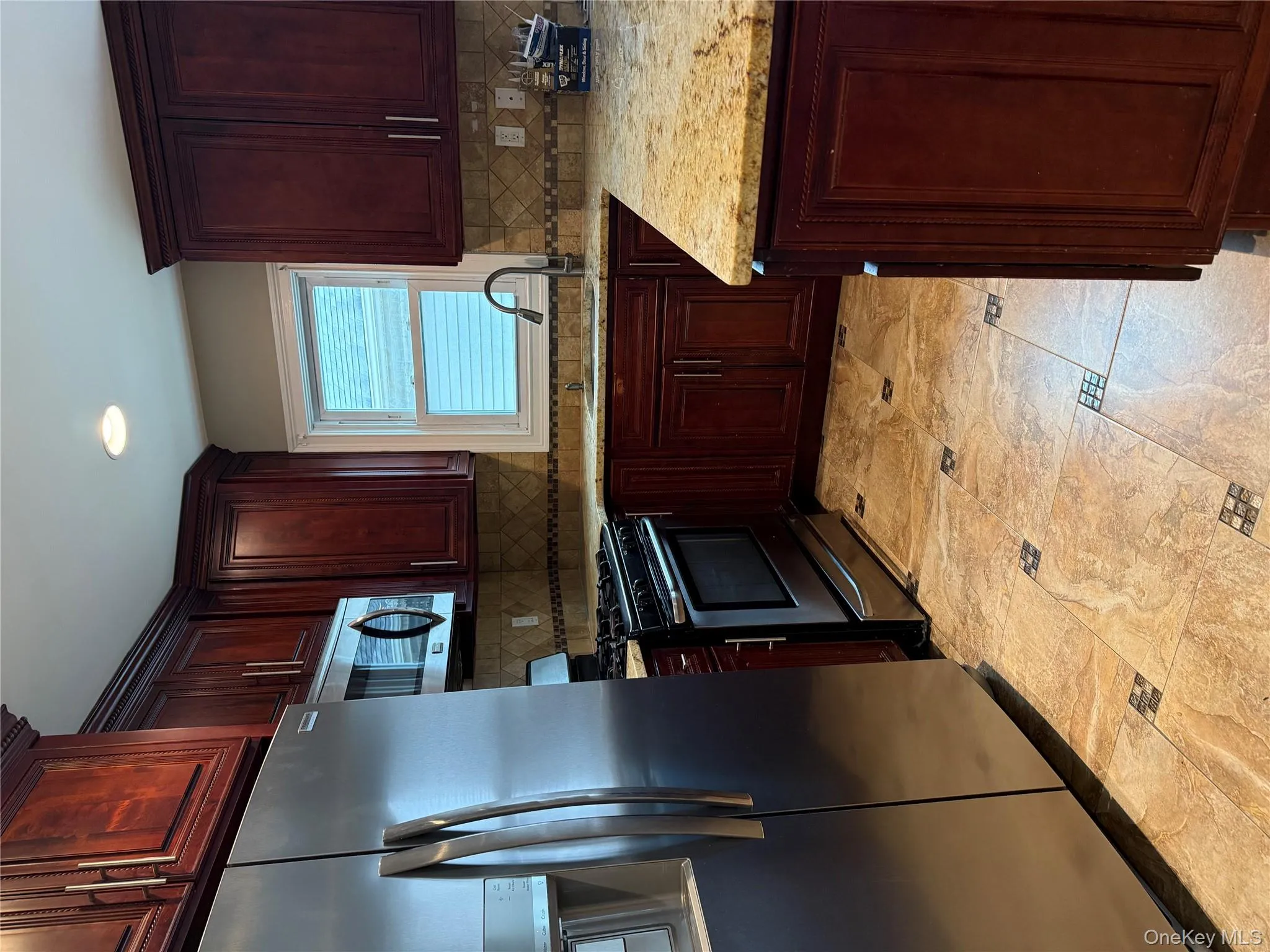Kitchen with stainless steel fridge, stove, light stone counters, reddish brown cabinets, and recessed lighting Kitchen with stainless steel fridge, stove, light stone counters, reddish brown cabinets, and recessed lighting