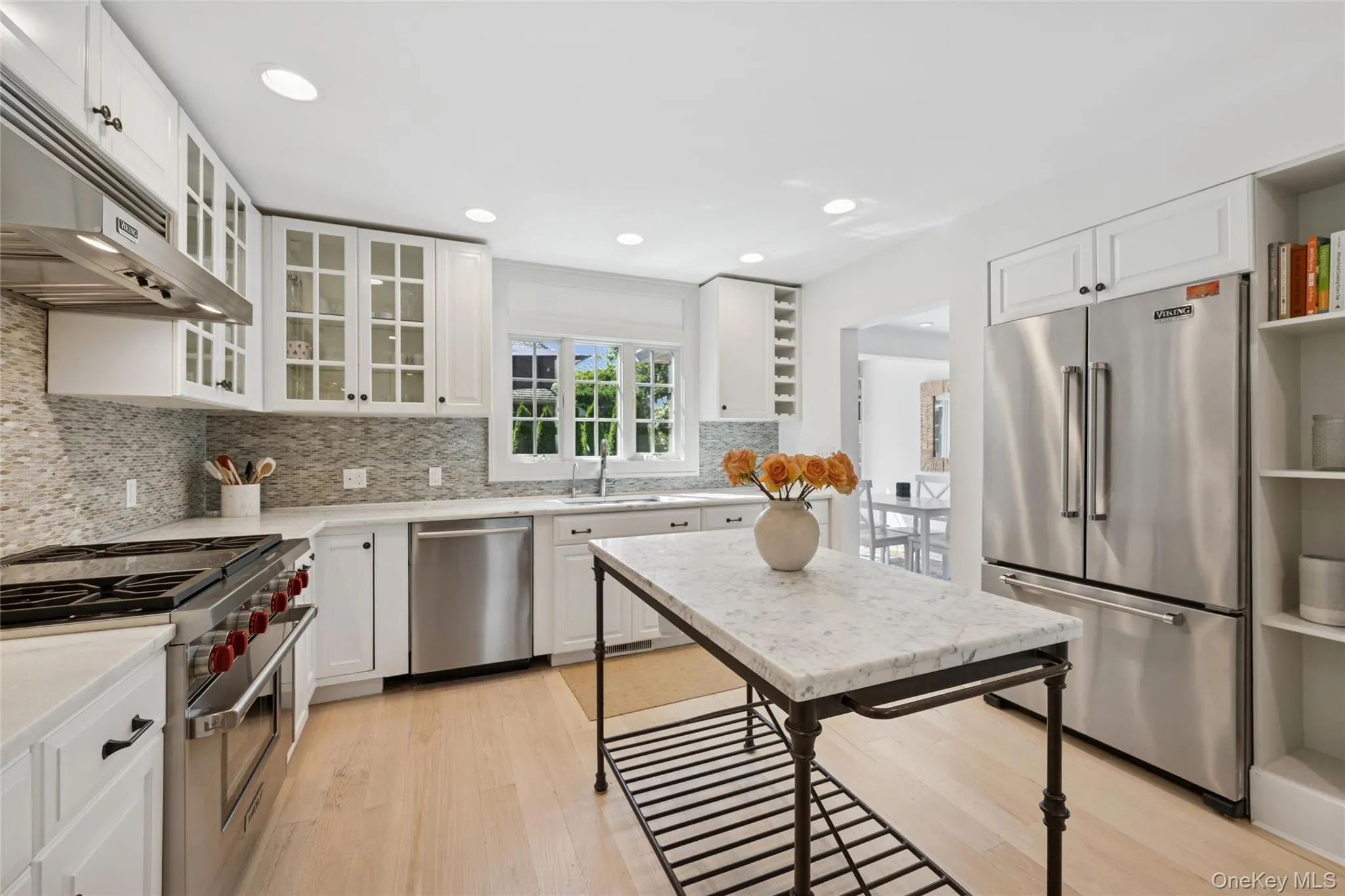 Kitchen with high end appliances, light wood-type flooring, tasteful backsplash, white cabinets, and under cabinet range hood Kitchen with high end appliances, light wood-type flooring, tasteful backsplash, white cabinets, and under cabinet range hood