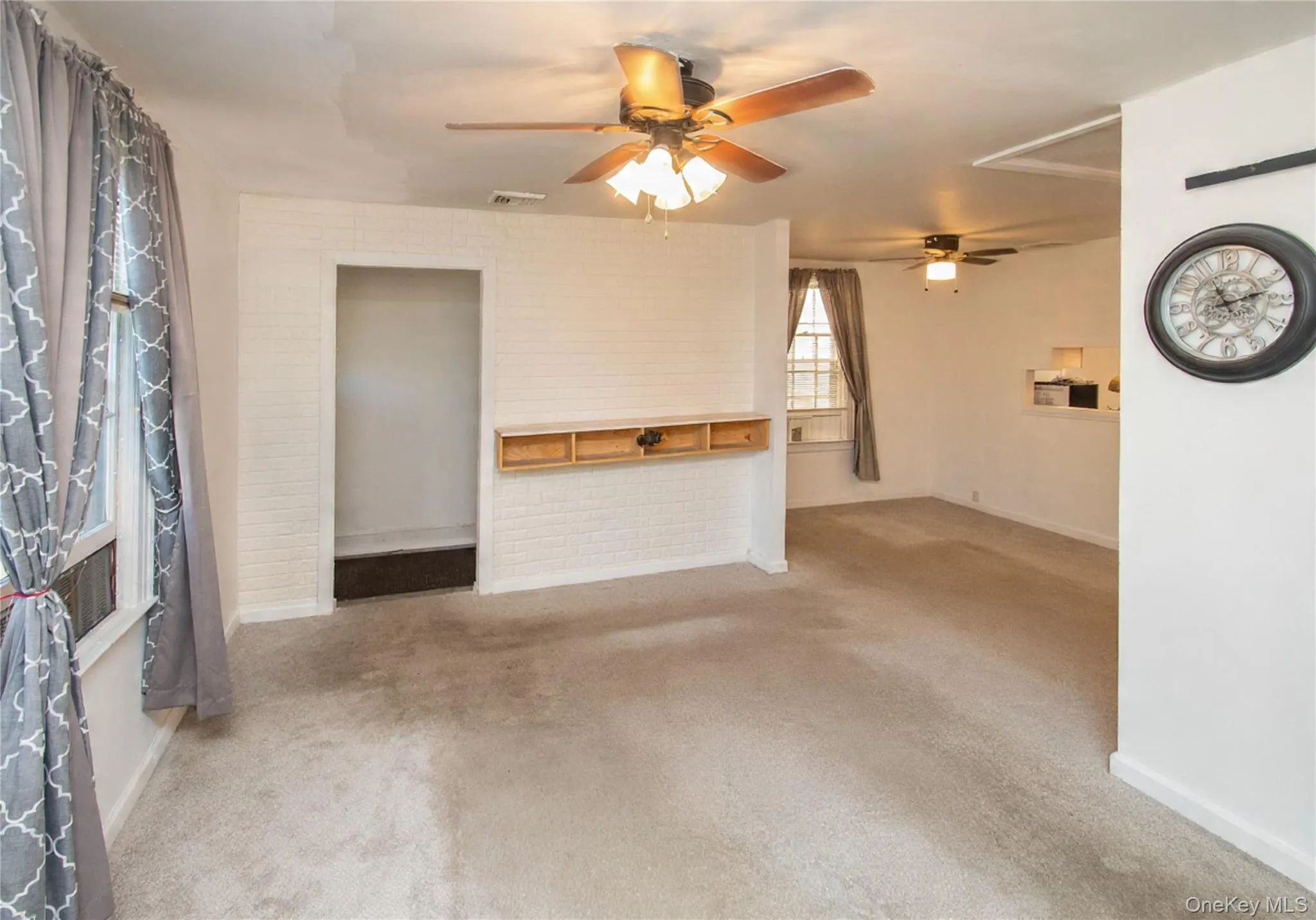 Unfurnished living room with carpet floors, ceiling fan, and brick wall Unfurnished living room with carpet floors, ceiling fan, and brick wall