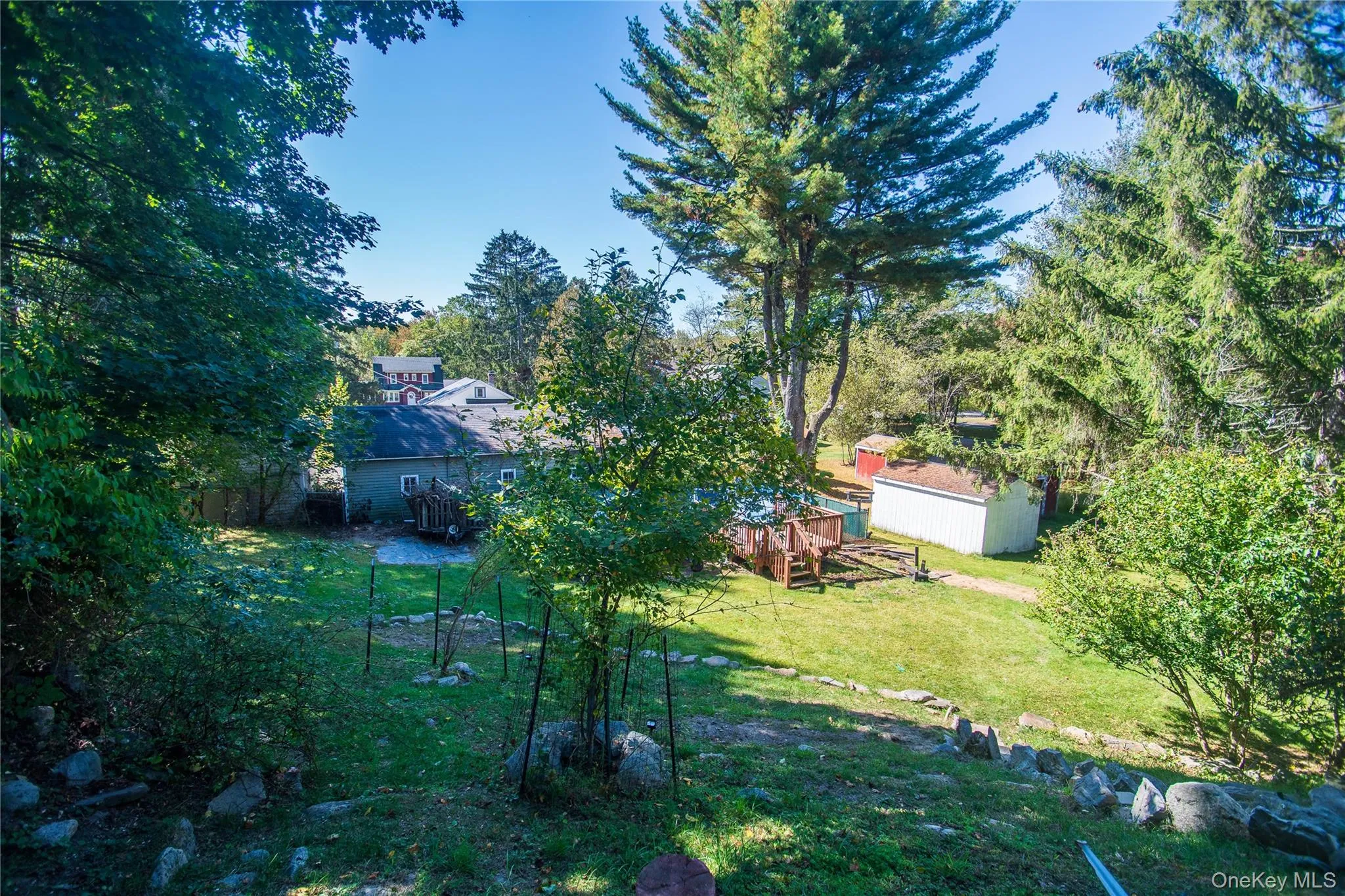 View of grassy yard with a wooden deck, view of wooded area, and a storage unit View of grassy yard with a wooden deck, view of wooded area, and a storage unit