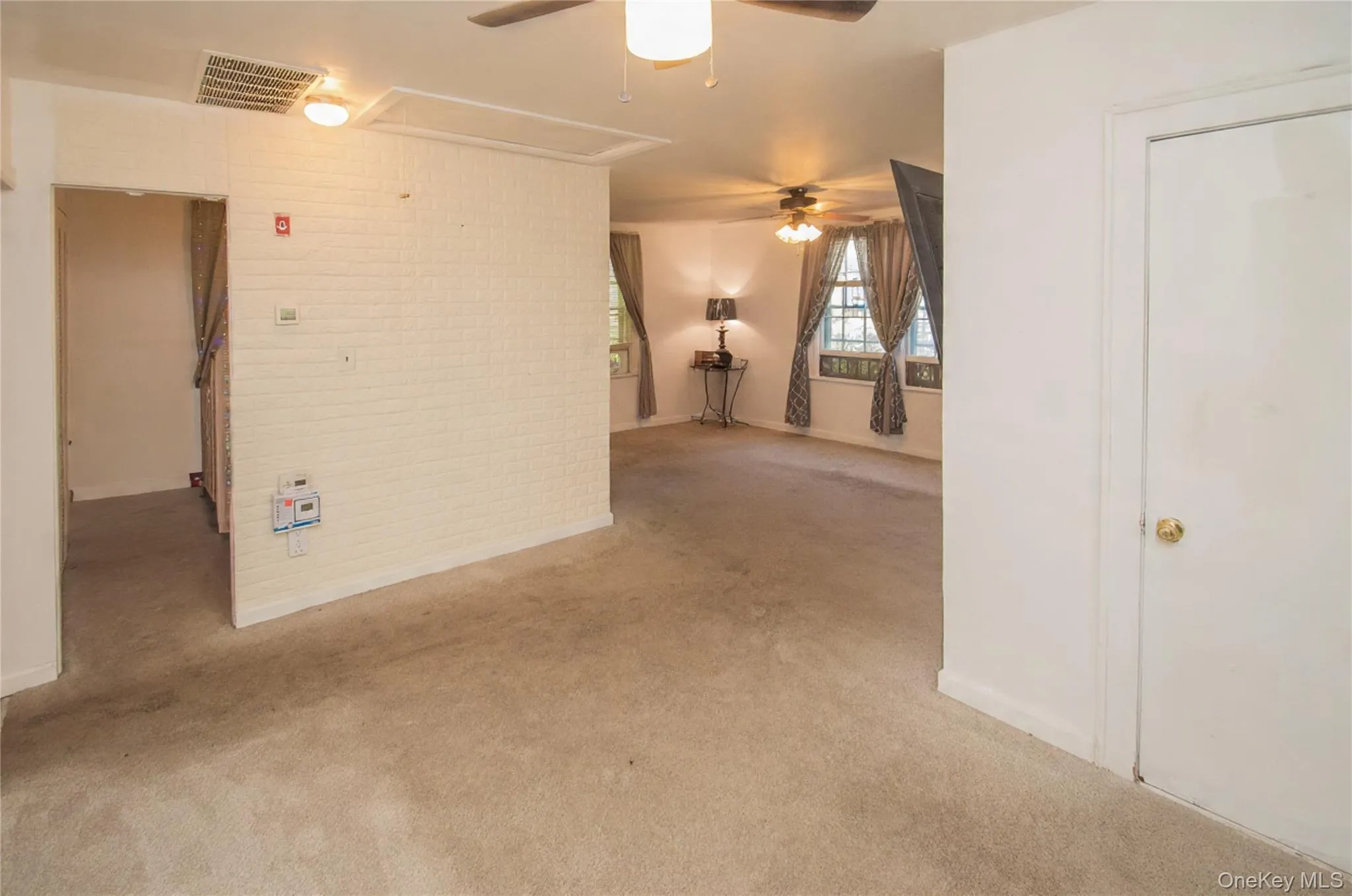 Carpeted spare room featuring attic access, brick wall, and ceiling fan Carpeted spare room featuring attic access, brick wall, and ceiling fan