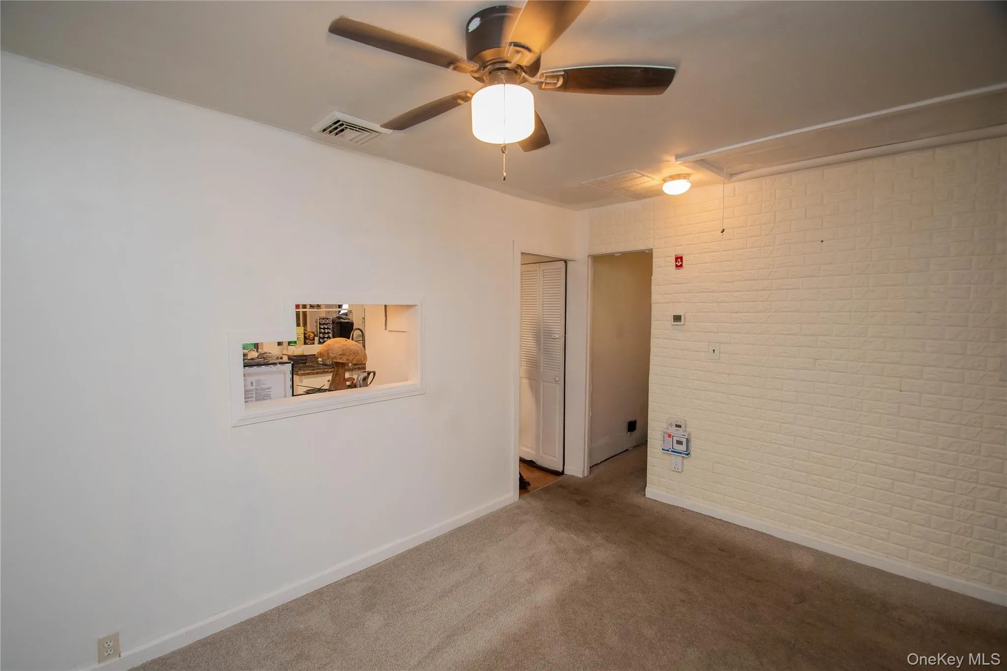 Unfurnished room featuring attic access, brick wall, carpet, and ceiling fan Unfurnished room featuring attic access, brick wall, carpet, and ceiling fan