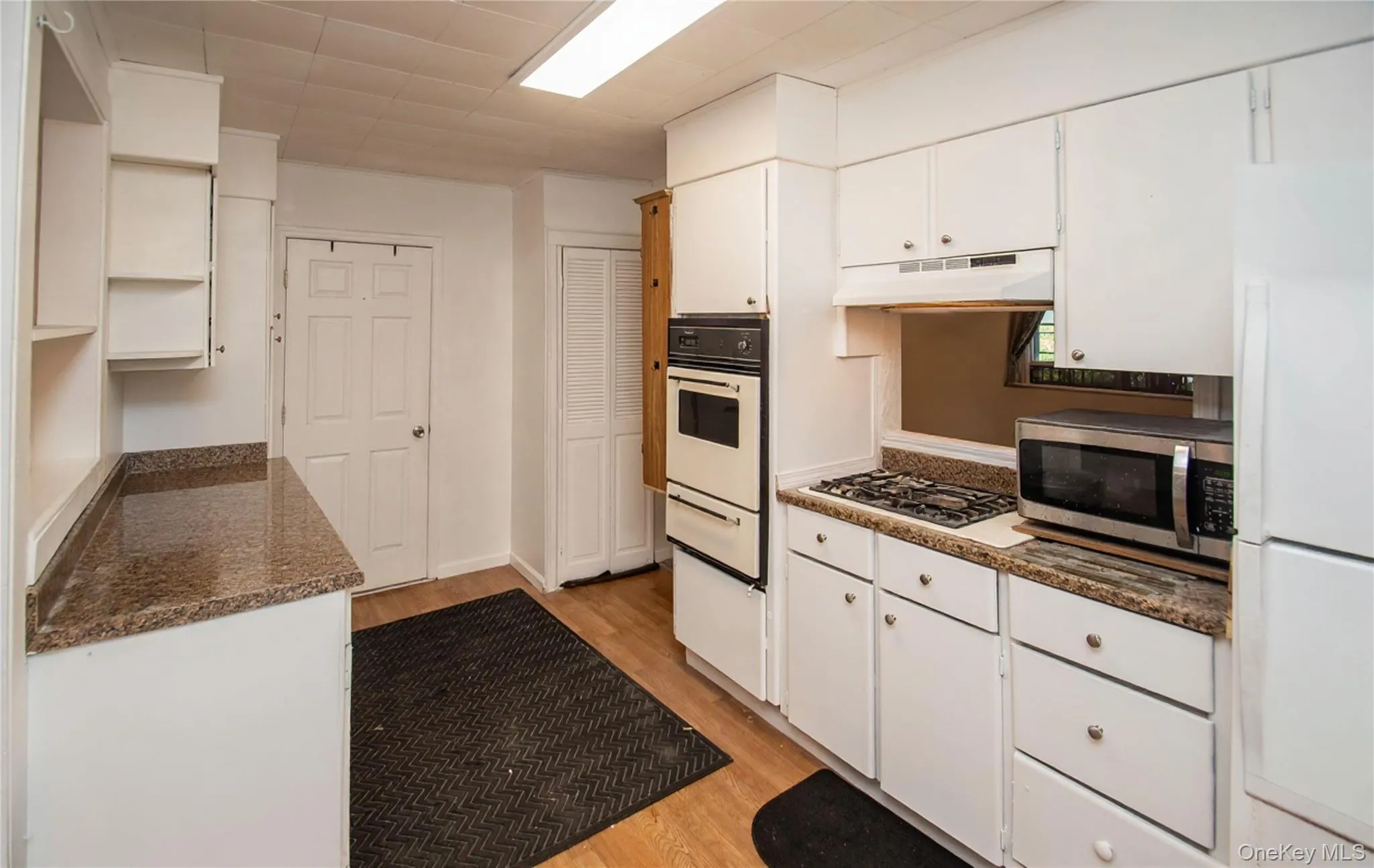 Kitchen with white cabinets, white appliances, light wood-type flooring, a warming drawer, and under cabinet range hood Kitchen with white cabinets, white appliances, light wood-type flooring, a warming drawer, and under cabinet range hood
