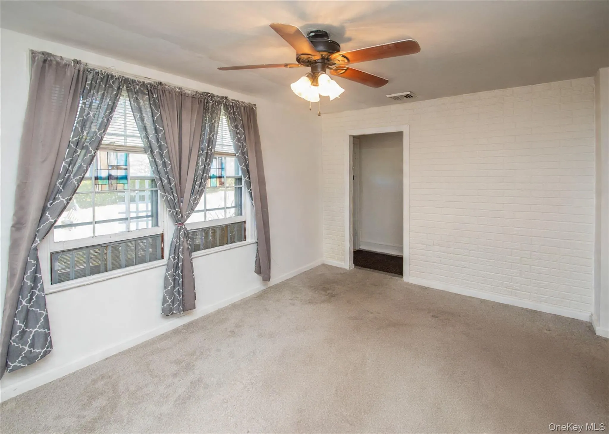 Carpeted spare room featuring brick wall and ceiling fan Carpeted spare room featuring brick wall and ceiling fan