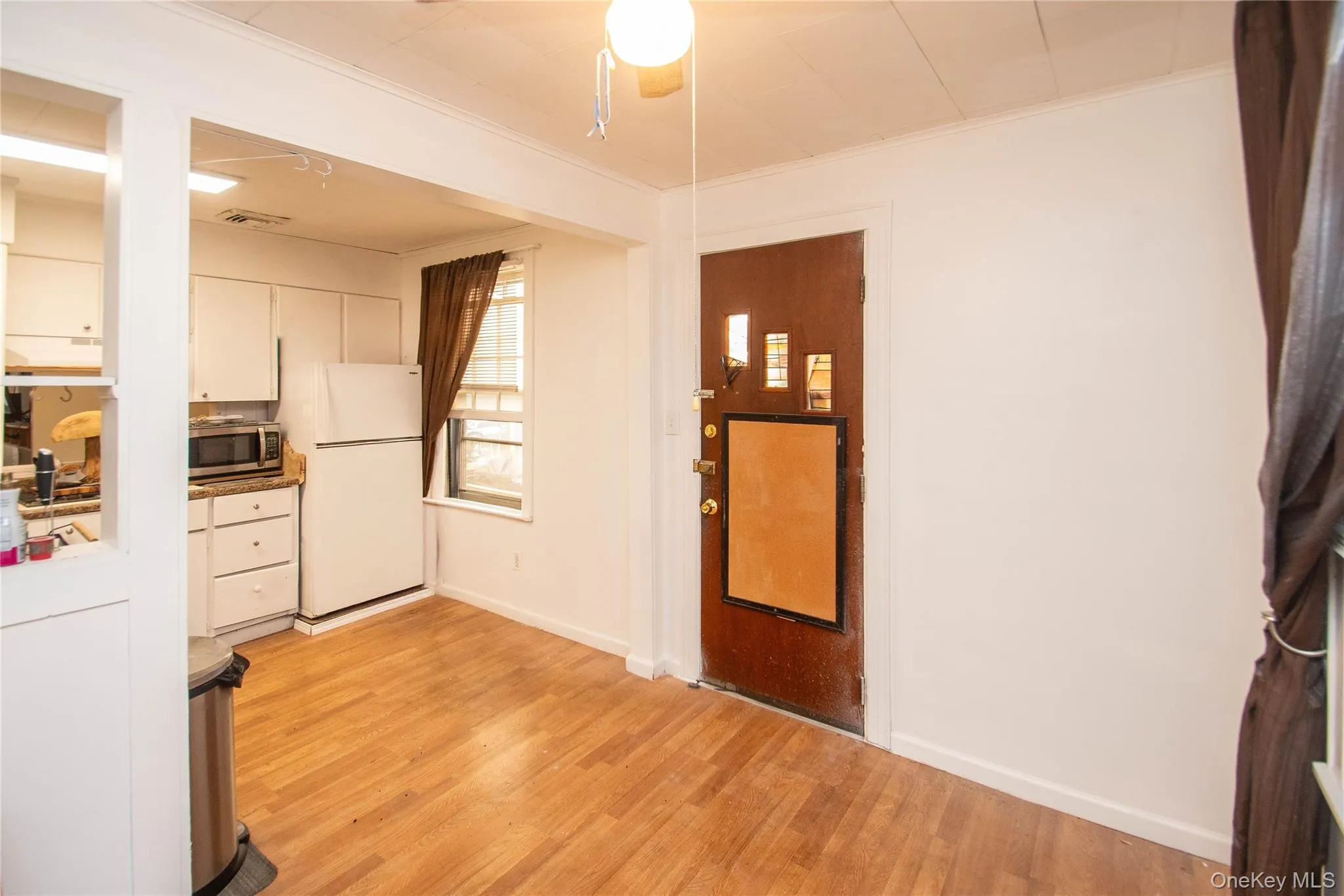 Kitchen with light wood-type flooring, freestanding refrigerator, white cabinetry, stainless steel microwave, and crown molding Kitchen with light wood-type flooring, freestanding refrigerator, white cabinetry, stainless steel microwave, and crown molding