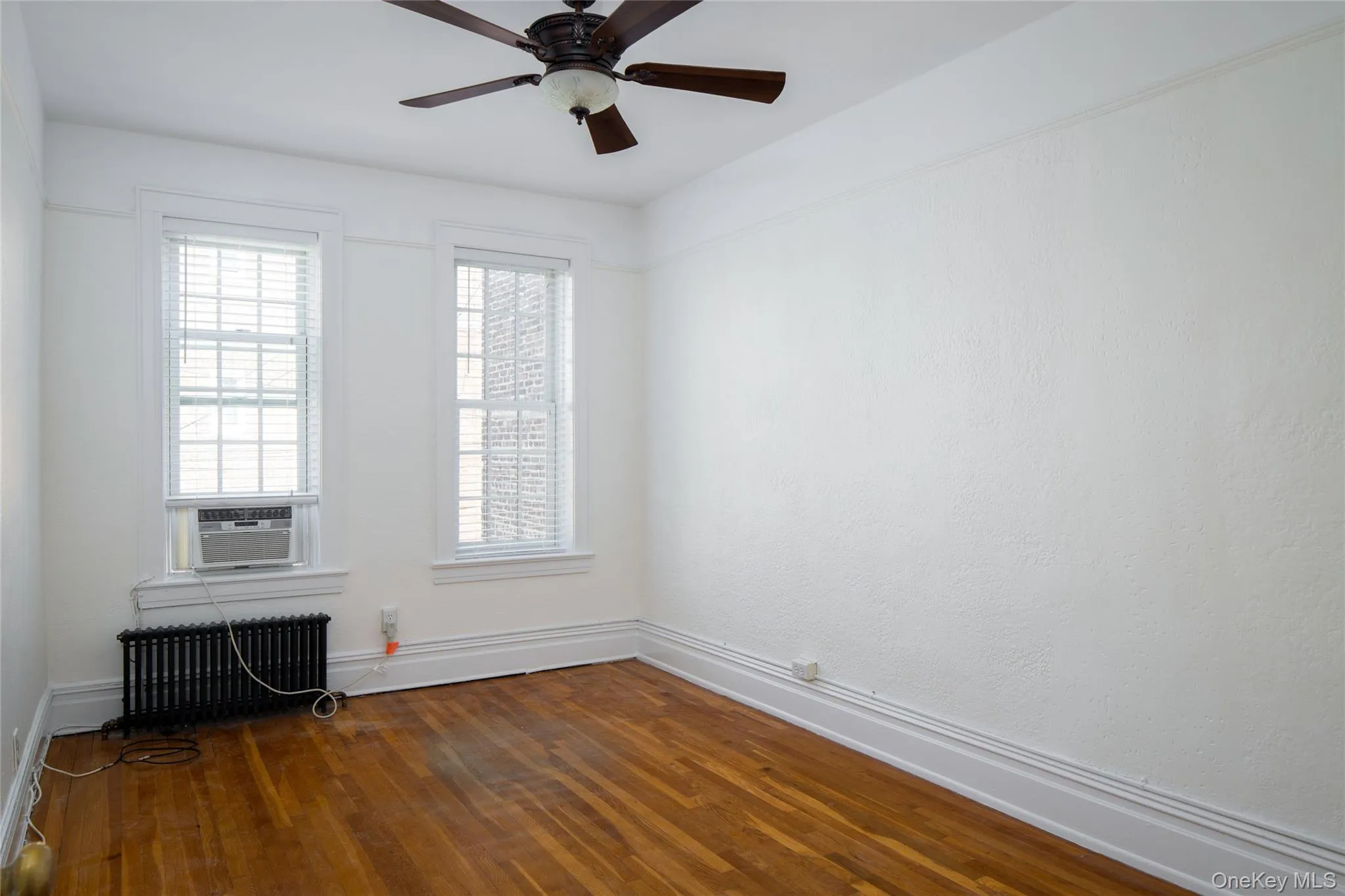 Spare room with dark wood-type flooring, radiator, and ceiling fan Spare room with dark wood-type flooring, radiator, and ceiling fan