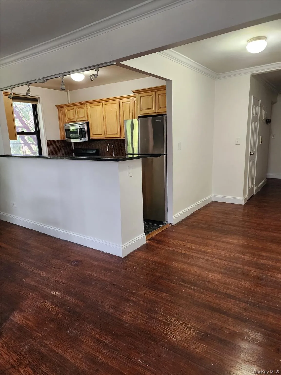 Kitchen featuring ornamental molding, appliances with stainless steel finishes, dark wood-style flooring, backsplash, and a peninsula Kitchen featuring ornamental molding, appliances with stainless steel finishes, dark wood-style flooring, backsplash, and a peninsula