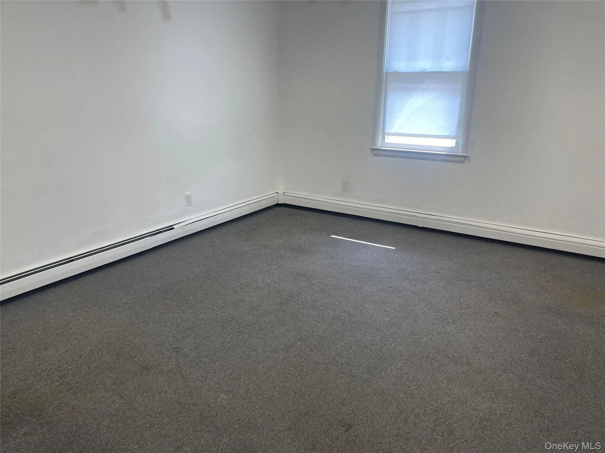Office room featuring a baseboard heating unit and dark carpet Office room featuring a baseboard heating unit and dark carpet