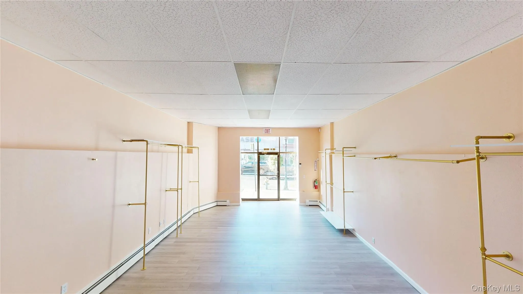 Hallway with a baseboard heating unit, a drop ceiling, and light wood-style floors Hallway with a baseboard heating unit, a drop ceiling, and light wood-style floors