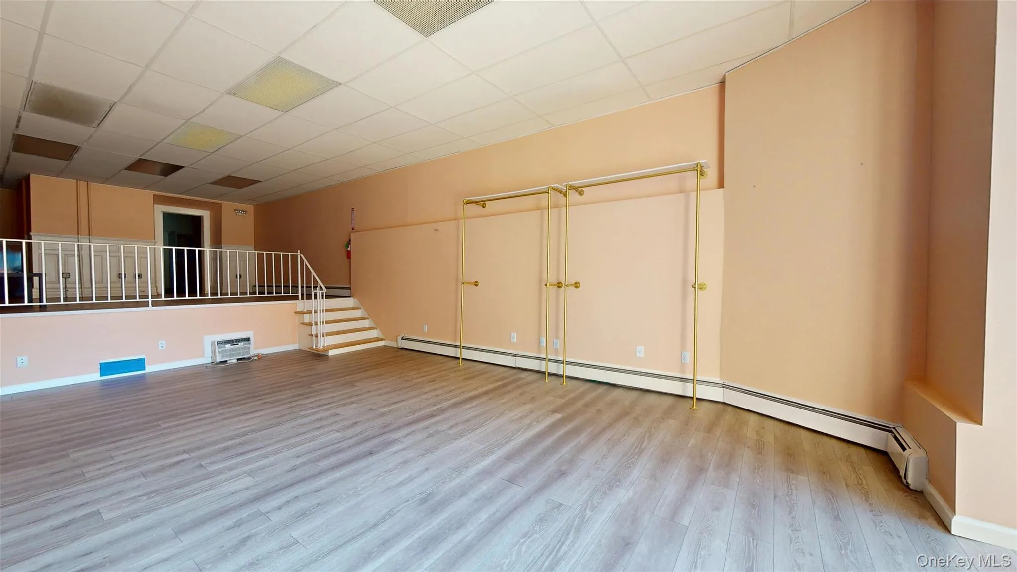 Unfurnished room with baseboard heating, stairway, a drop ceiling, and light wood-type flooring Unfurnished room with baseboard heating, stairway, a drop ceiling, and light wood-type flooring
