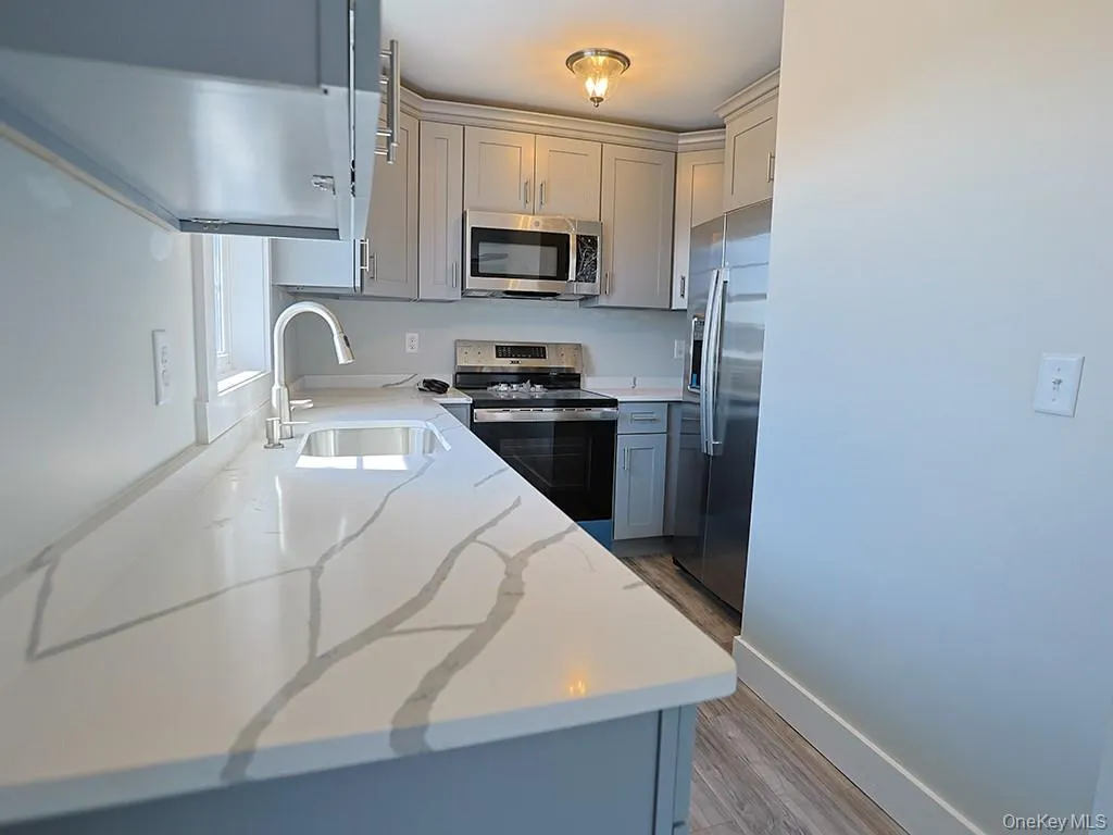 Kitchen featuring stainless steel appliances, gray cabinets, light wood finished floors, and light stone countertops Kitchen featuring stainless steel appliances, gray cabinets, light wood finished floors, and light stone countertops