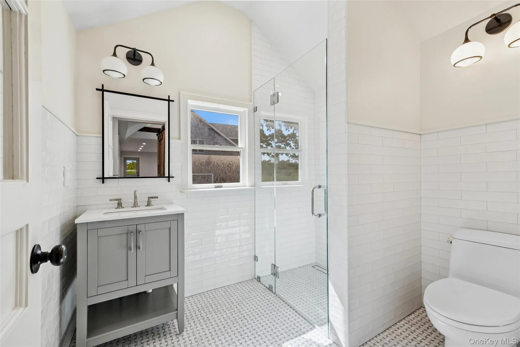Bathroom with tile walls, vanity, a stall shower, a wainscoted wall, and vaulted ceiling Bathroom with tile walls, vanity, a stall shower, a wainscoted wall, and vaulted ceiling