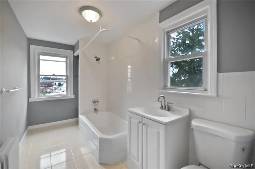 Full bathroom featuring bathtub / shower combination, radiator heating unit, vanity, and plenty of natural light Full bathroom featuring bathtub / shower combination, radiator heating unit, vanity, and plenty of natural light