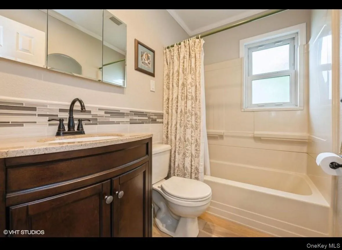 Bathroom featuring shower / bath combo with shower curtain, vanity, tile walls, ornamental molding, and wainscoting Bathroom featuring shower / bath combo with shower curtain, vanity, tile walls, ornamental molding, and wainscoting