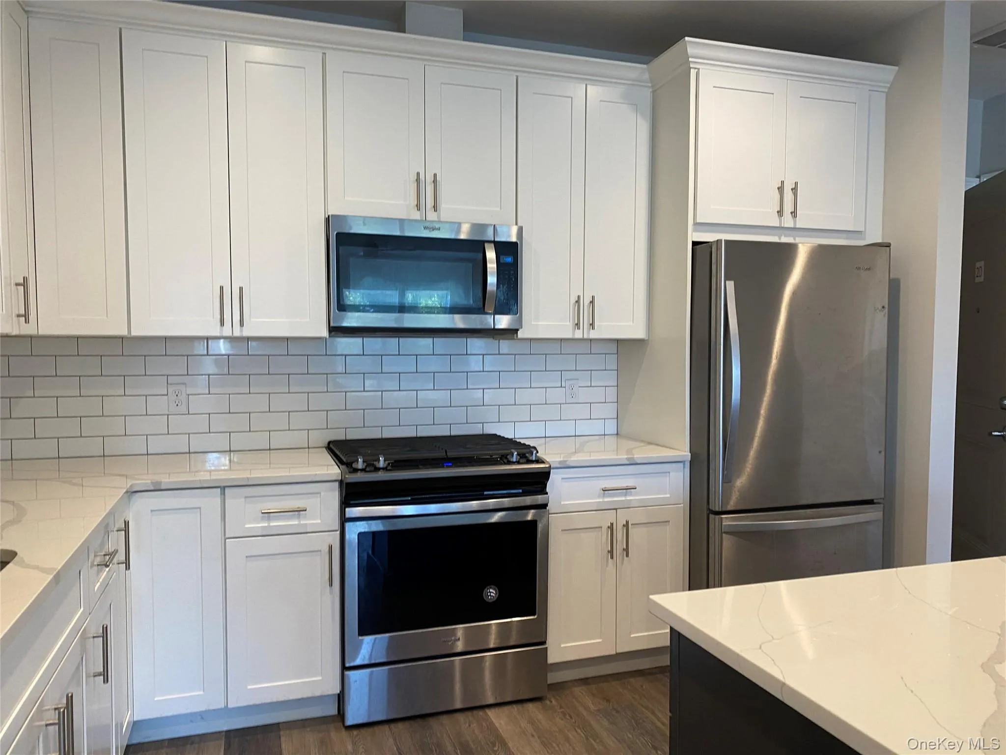 Kitchen with appliances with stainless steel finishes, white cabinetry, light stone countertops, dark wood-type flooring, and decorative backsplash Kitchen with appliances with stainless steel finishes, white cabinetry, light stone countertops, dark wood-type flooring, and decorative backsplash