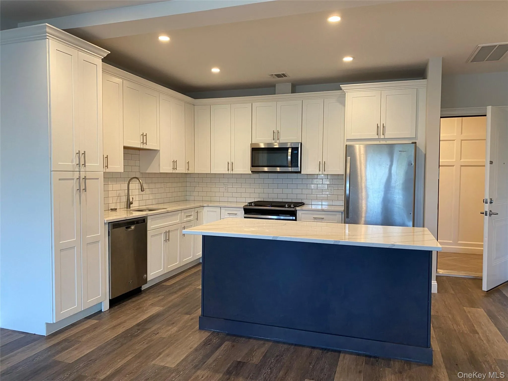 Kitchen with appliances with stainless steel finishes, a center island, recessed lighting, white cabinetry, and light stone countertops Kitchen with appliances with stainless steel finishes, a center island, recessed lighting, white cabinetry, and light stone countertops