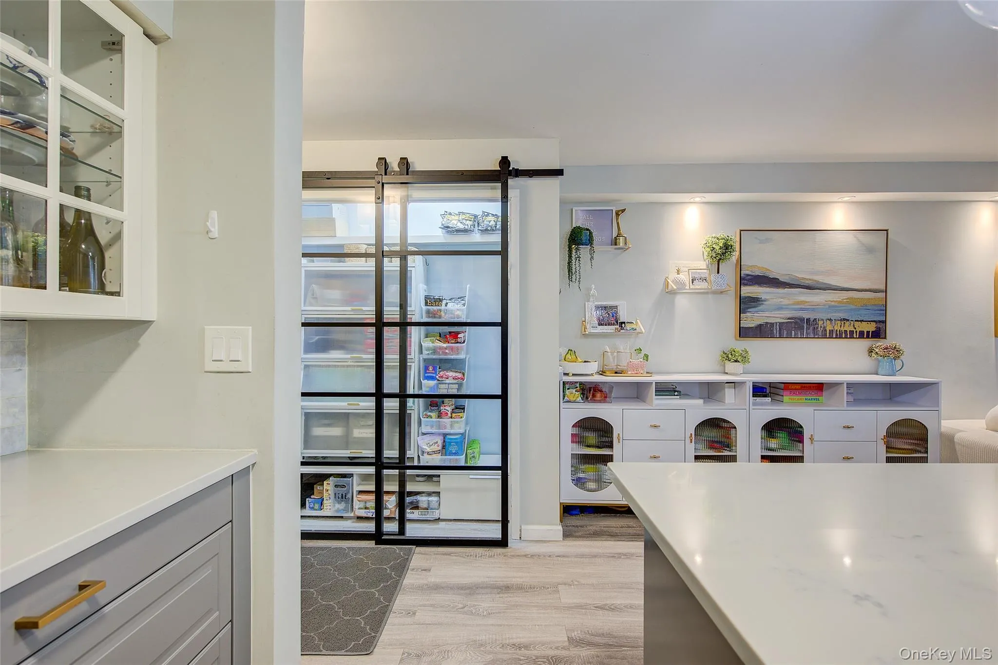 Kitchen with light wood-style floors, glass insert cabinets, gray cabinetry, and light stone countertops Kitchen with light wood-style floors, glass insert cabinets, gray cabinetry, and light stone countertops