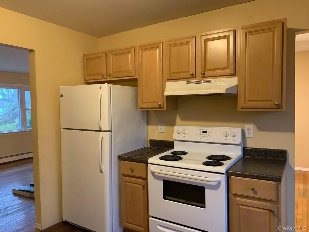 Kitchen with dark countertops, white appliances, dark wood finished floors, and under cabinet range hood Kitchen with dark countertops, white appliances, dark wood finished floors, and under cabinet range hood