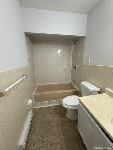 Bathroom with tile walls, wainscoting, vanity, washtub / shower combination, and baseboard heating Bathroom with tile walls, wainscoting, vanity, washtub / shower combination, and baseboard heating