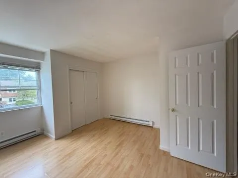 Unfurnished bedroom featuring light wood-style floors, a baseboard heating unit, and a closet Unfurnished bedroom featuring light wood-style floors, a baseboard heating unit, and a closet