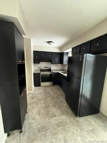 Kitchen with dark cabinets, freestanding refrigerator, stainless steel range with electric stovetop, decorative backsplash, and open shelves Kitchen with dark cabinets, freestanding refrigerator, stainless steel range with electric stovetop, decorative backsplash, and open shelves