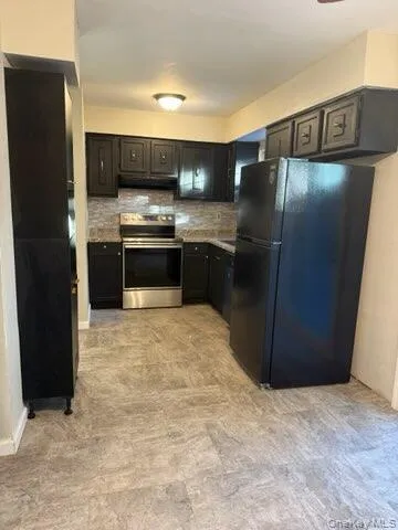 Kitchen with freestanding refrigerator, backsplash, stainless steel range with electric cooktop, and under cabinet range hood Kitchen with freestanding refrigerator, backsplash, stainless steel range with electric cooktop, and under cabinet range hood