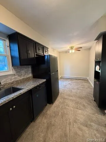 Kitchen featuring backsplash, black appliances, ceiling fan, dark cabinets, and a baseboard radiator Kitchen featuring backsplash, black appliances, ceiling fan, dark cabinets, and a baseboard radiator