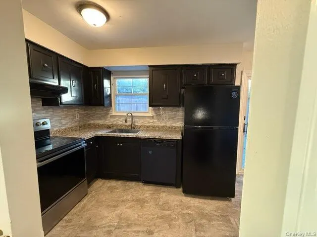 Kitchen featuring black appliances, backsplash, under cabinet range hood, and dark cabinets Kitchen featuring black appliances, backsplash, under cabinet range hood, and dark cabinets