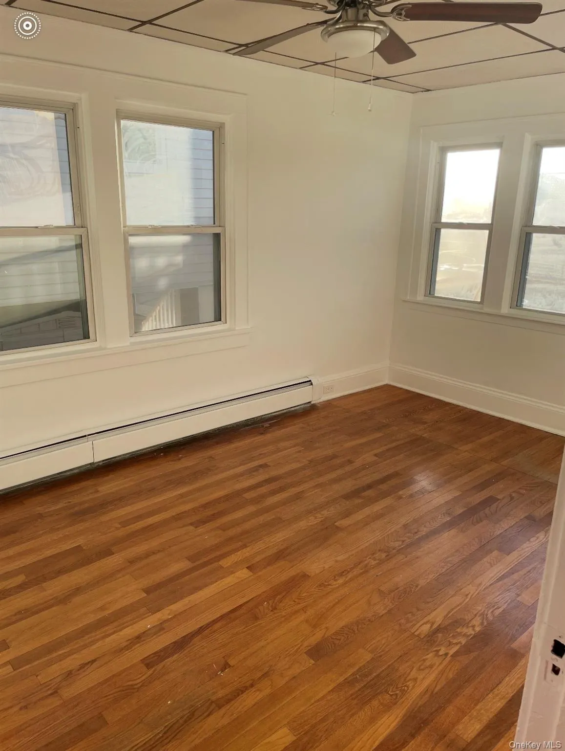 Spare room featuring dark wood-style floors, a baseboard heating unit, and ceiling fan Spare room featuring dark wood-style floors, a baseboard heating unit, and ceiling fan