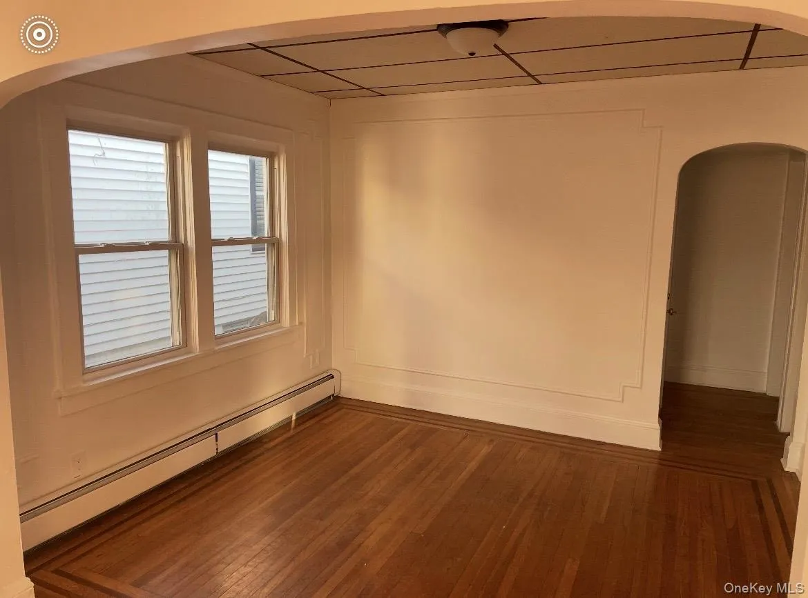 Spare room with arched walkways, a baseboard radiator, and dark wood-style floors Spare room with arched walkways, a baseboard radiator, and dark wood-style floors