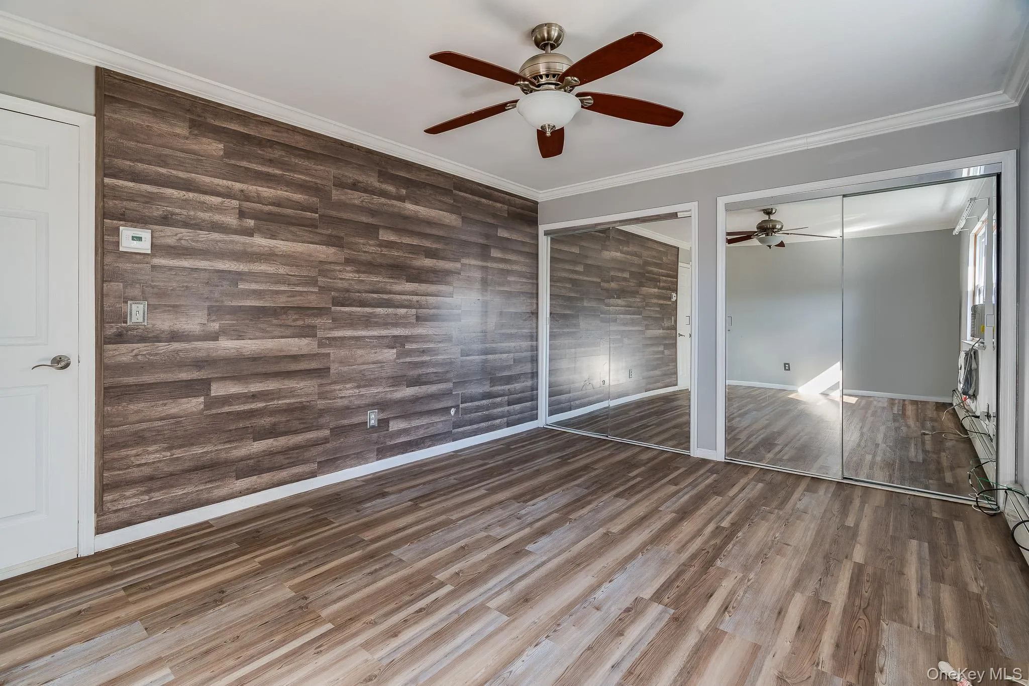 Unfurnished bedroom with crown molding, multiple closets, wood finished floors, ceiling fan, and wooden walls Unfurnished bedroom with crown molding, multiple closets, wood finished floors, ceiling fan, and wooden walls