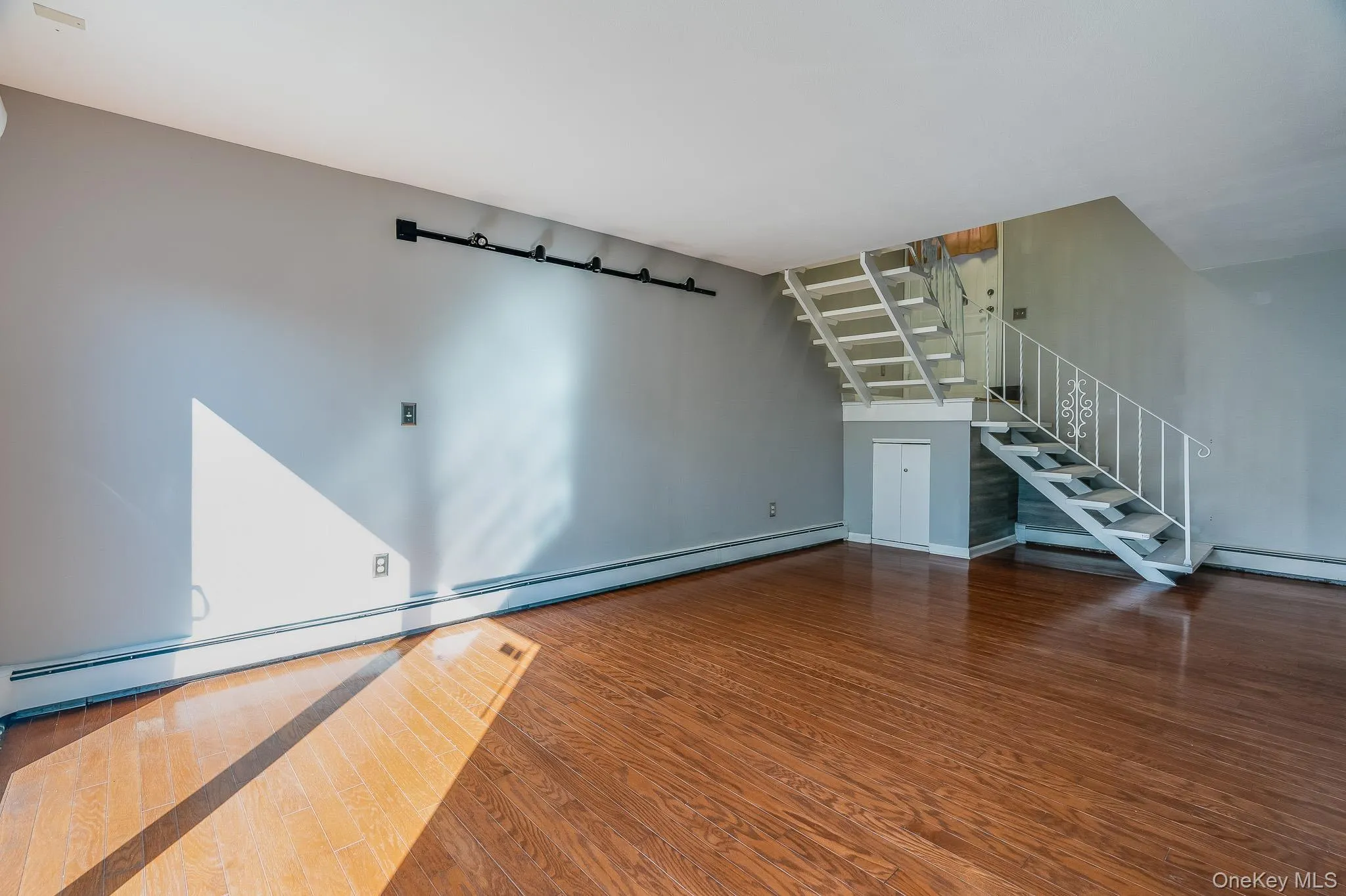 Unfurnished living room with a baseboard heating unit, wood finished floors, and stairs Unfurnished living room with a baseboard heating unit, wood finished floors, and stairs