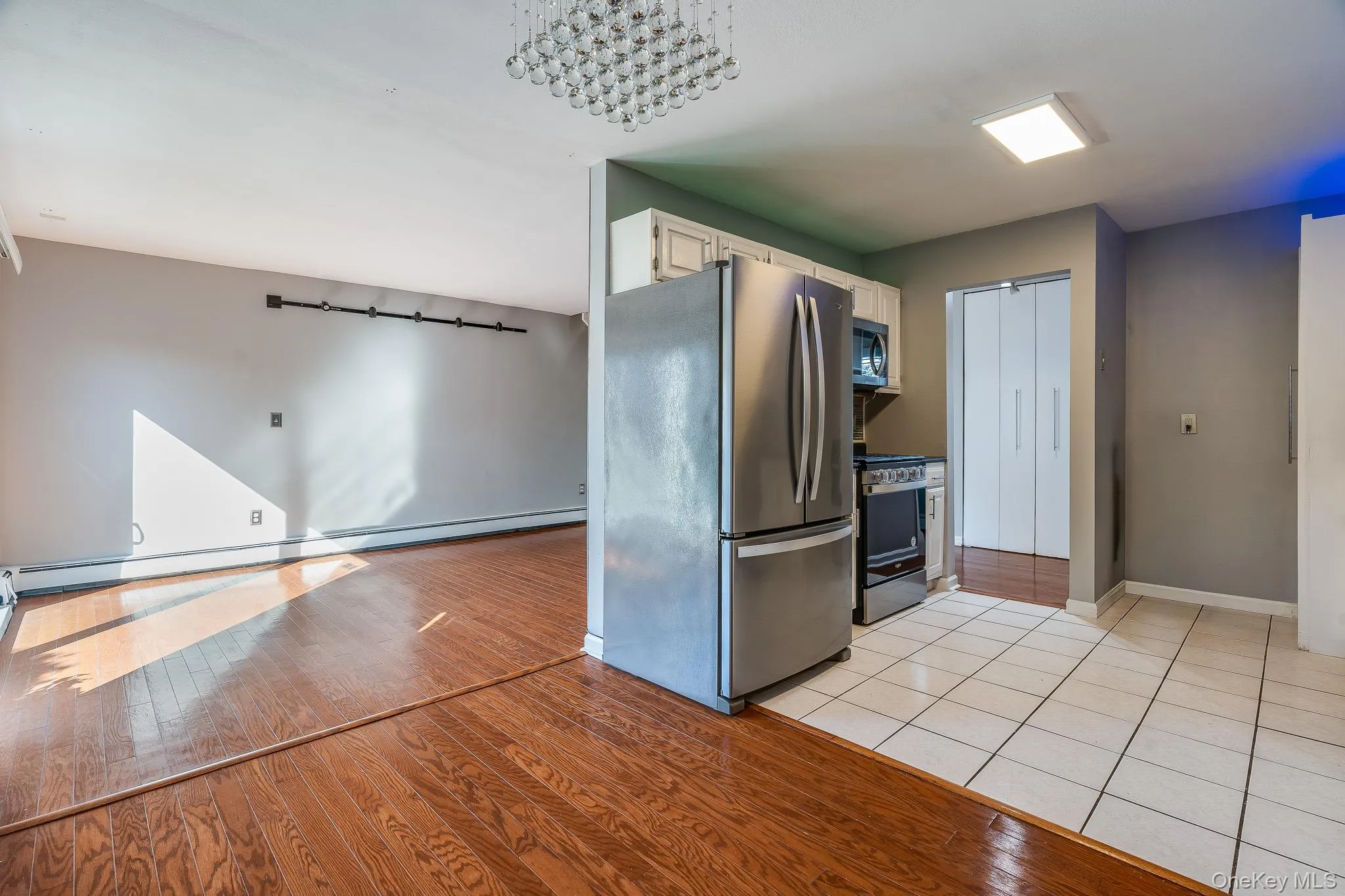 Kitchen featuring stainless steel appliances, light wood finished floors, a baseboard radiator, a chandelier, and white cabinetry Kitchen featuring stainless steel appliances, light wood finished floors, a baseboard radiator, a chandelier, and white cabinetry