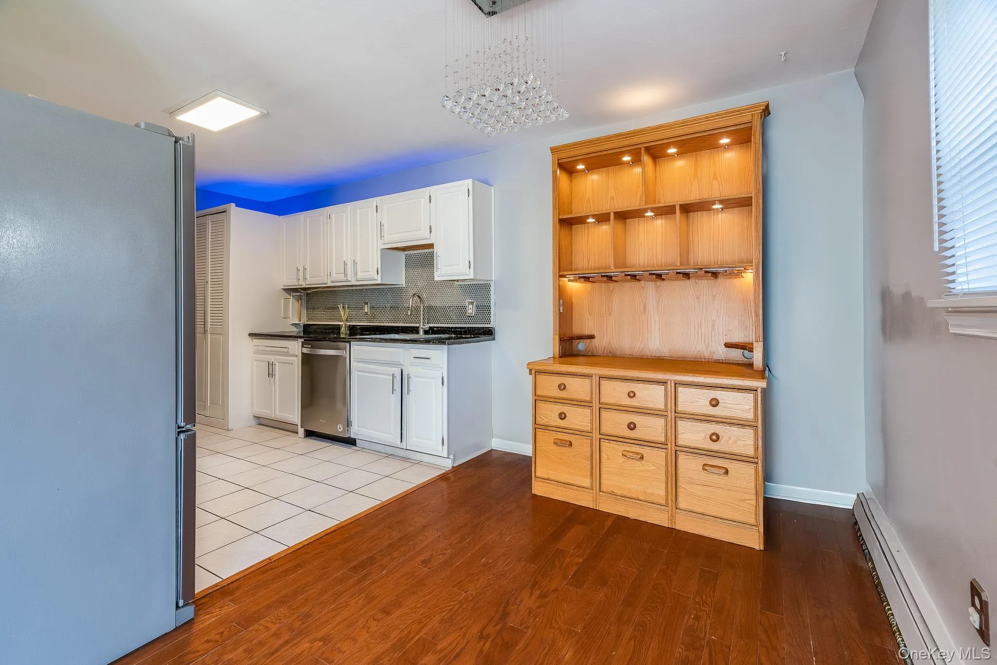 Kitchen featuring appliances with stainless steel finishes, decorative backsplash, a baseboard heating unit, white cabinets, and light wood finished floors Kitchen featuring appliances with stainless steel finishes, decorative backsplash, a baseboard heating unit, white cabinets, and light wood finished floors