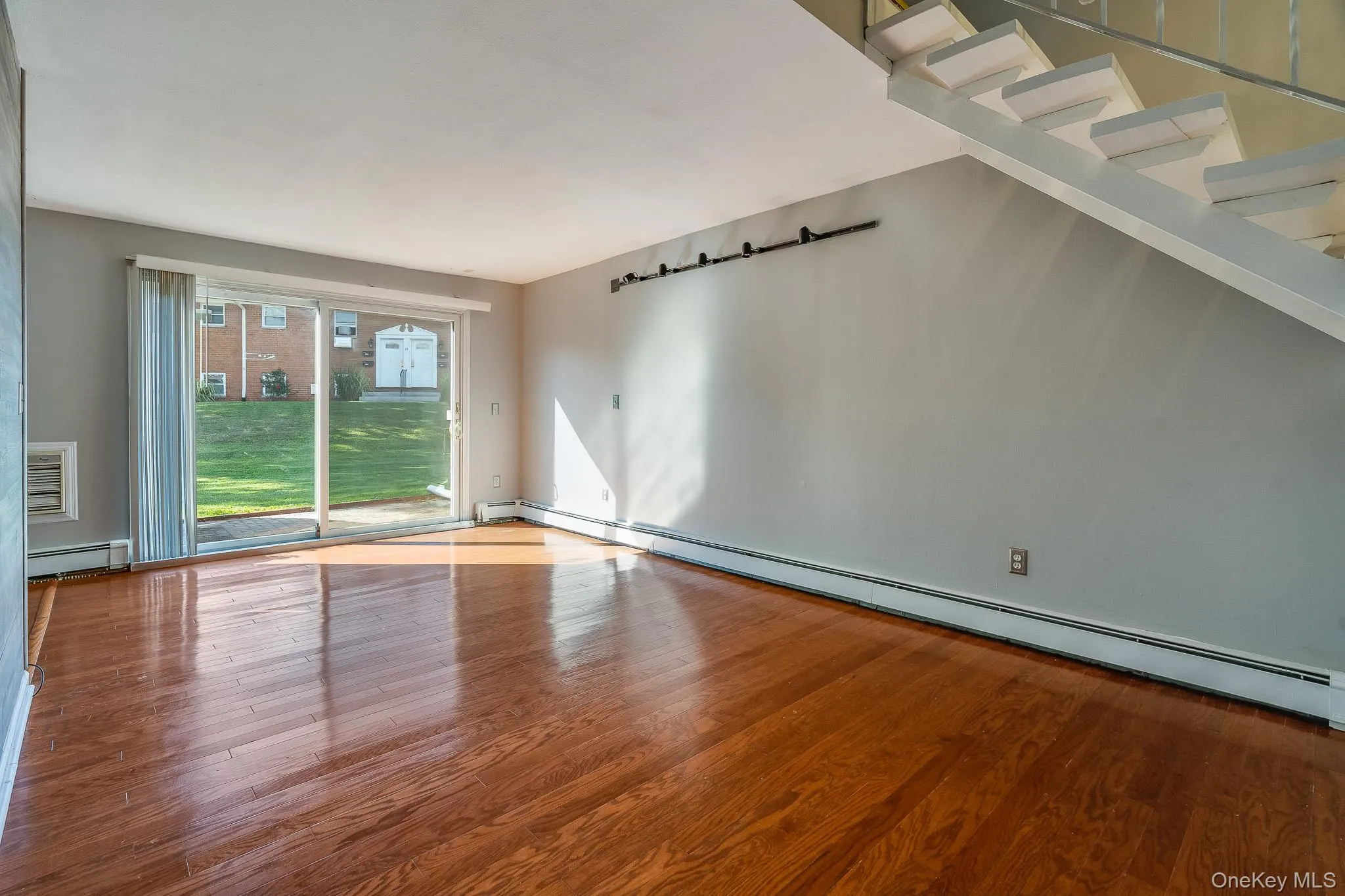 Empty room featuring baseboard heating, wood finished floors, and a wall unit AC Empty room featuring baseboard heating, wood finished floors, and a wall unit AC