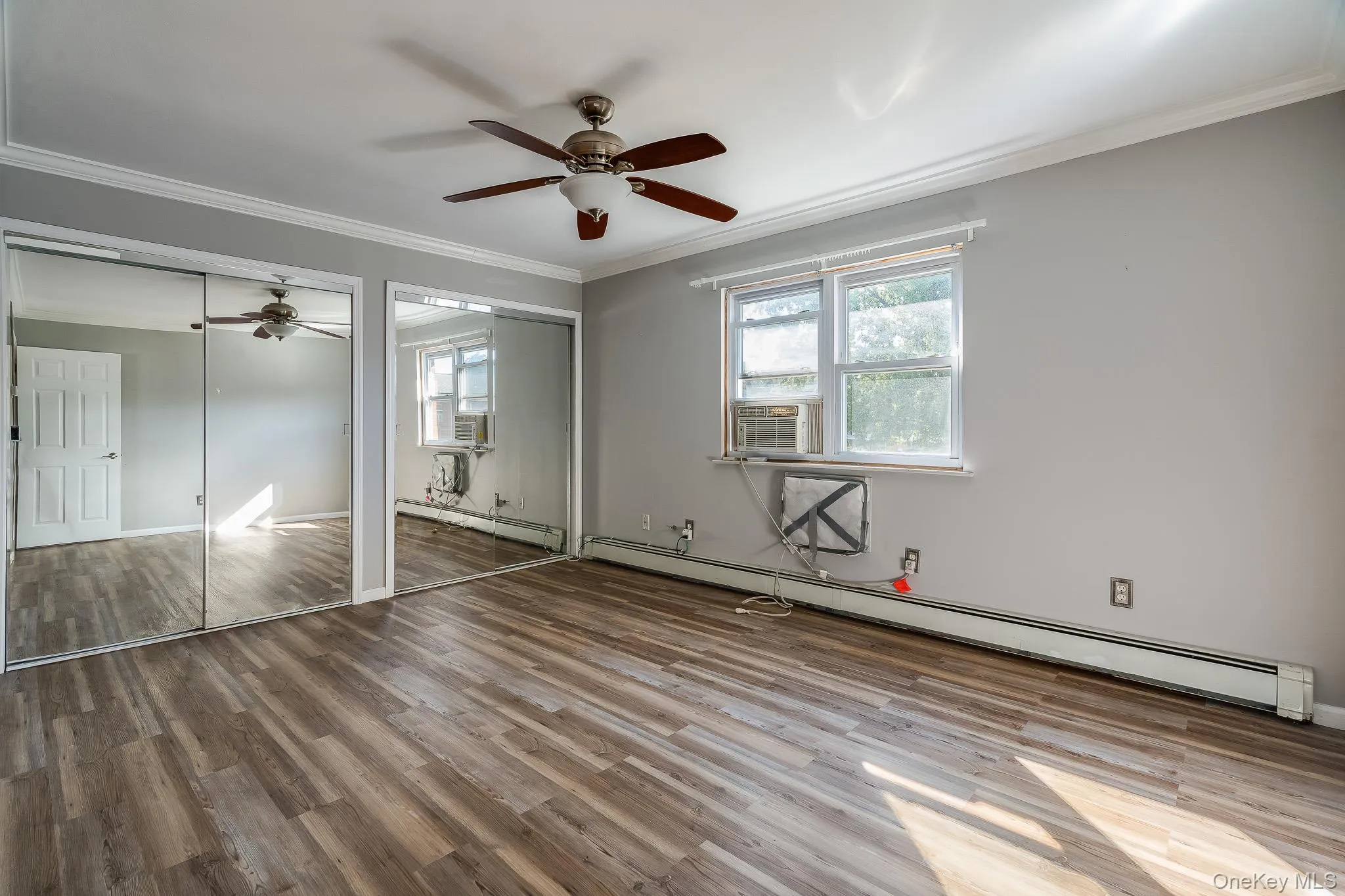 Unfurnished bedroom featuring ornamental molding, baseboard heating, multiple closets, light wood-style floors, and a ceiling fan Unfurnished bedroom featuring ornamental molding, baseboard heating, multiple closets, light wood-style floors, and a ceiling fan